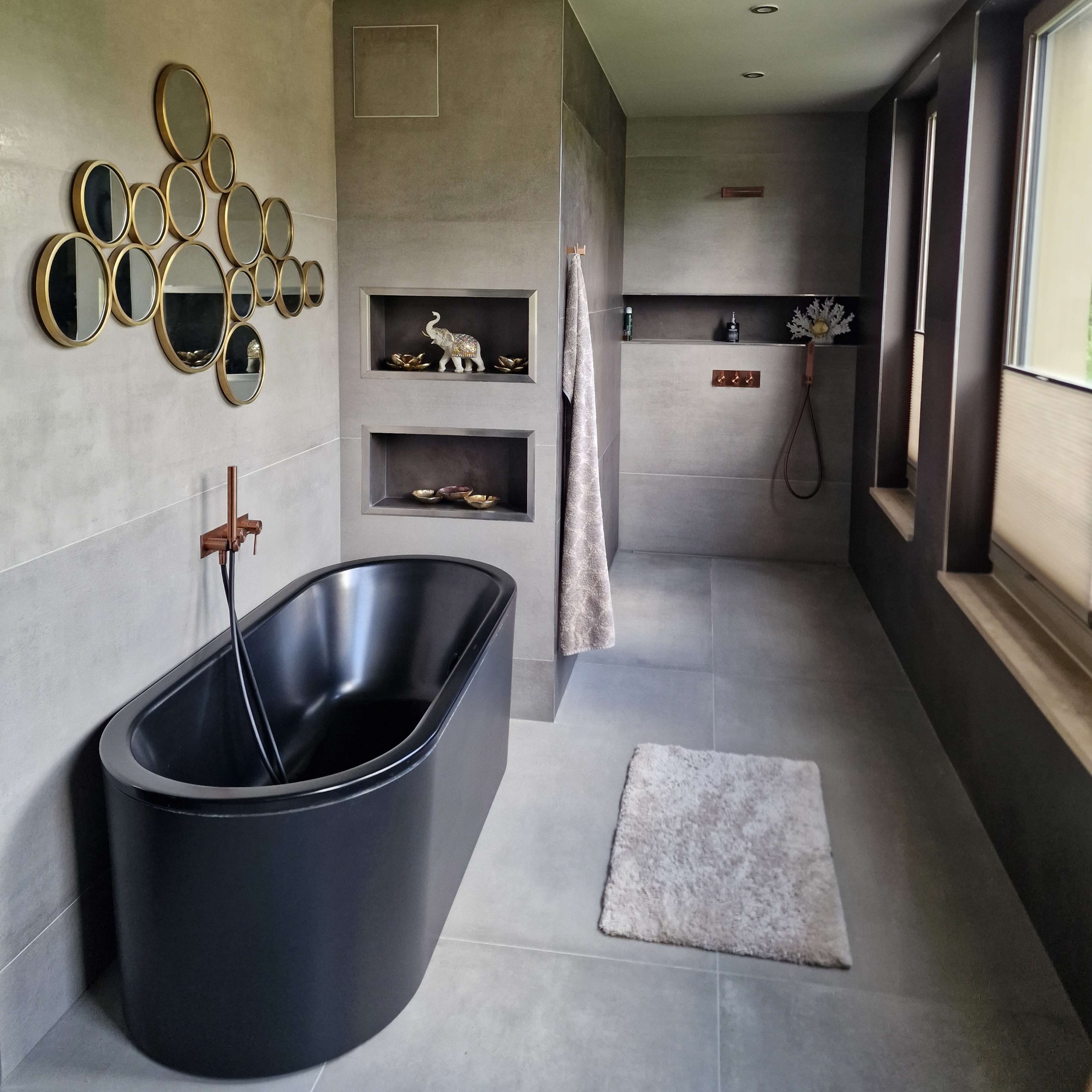 A modern bathroom featuring a black freestanding bathtub, gray tiled walls, and a series of round mirrors on one wall.