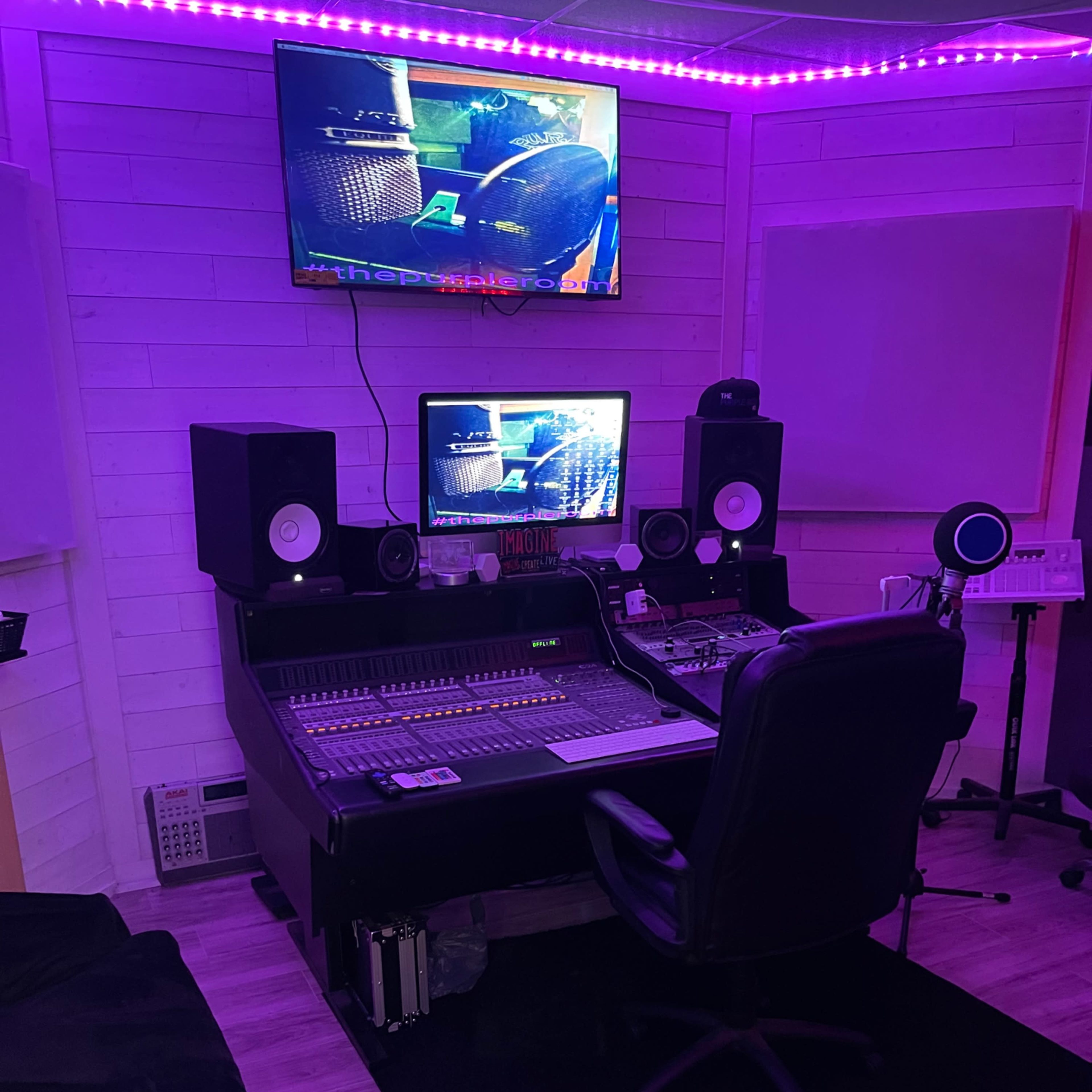 A music production studio featuring a mixing console, speakers, and dual monitors under purple LED lights.