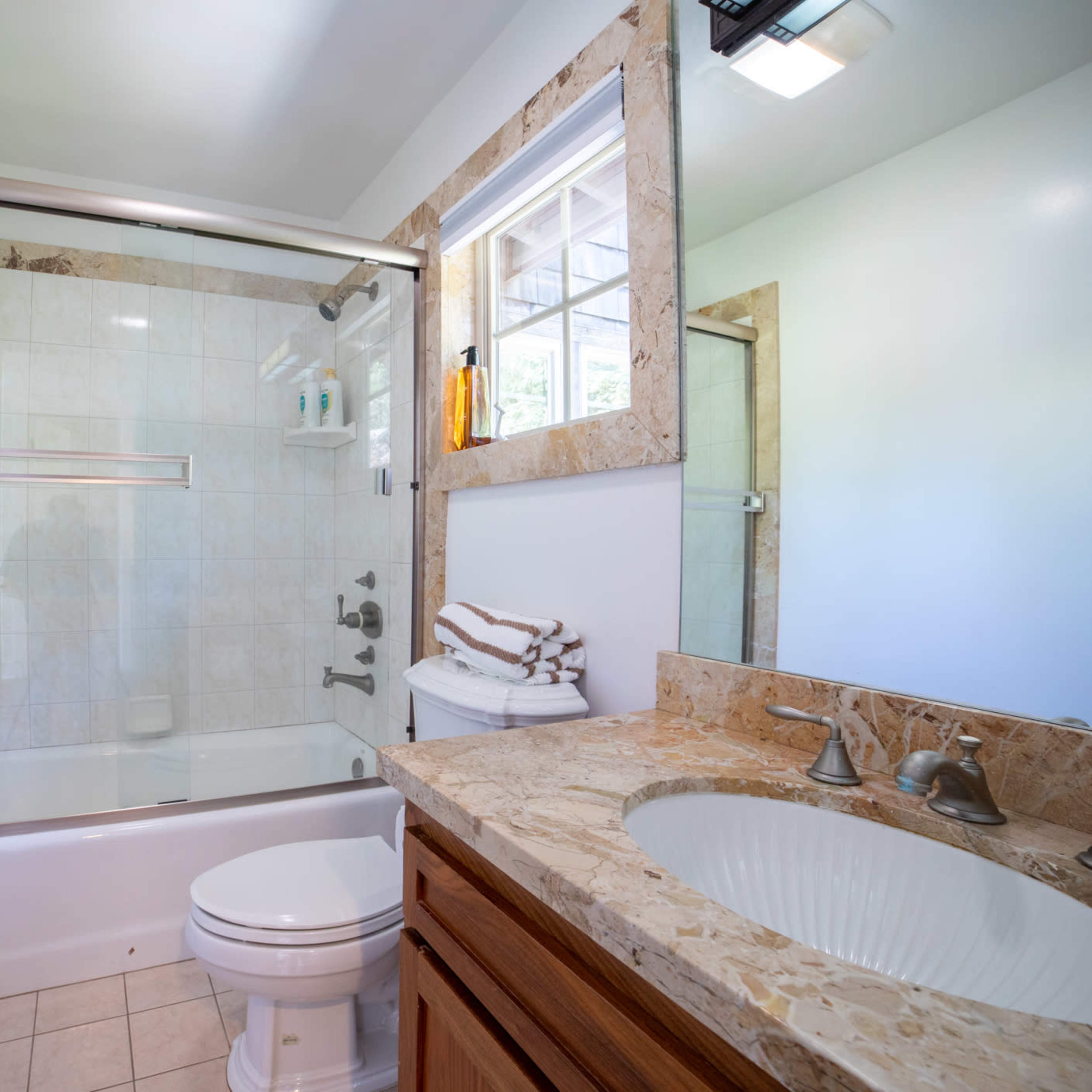 A modern bathroom featuring a shower-tub combination, a vanity with a sink, and neatly stacked towels.