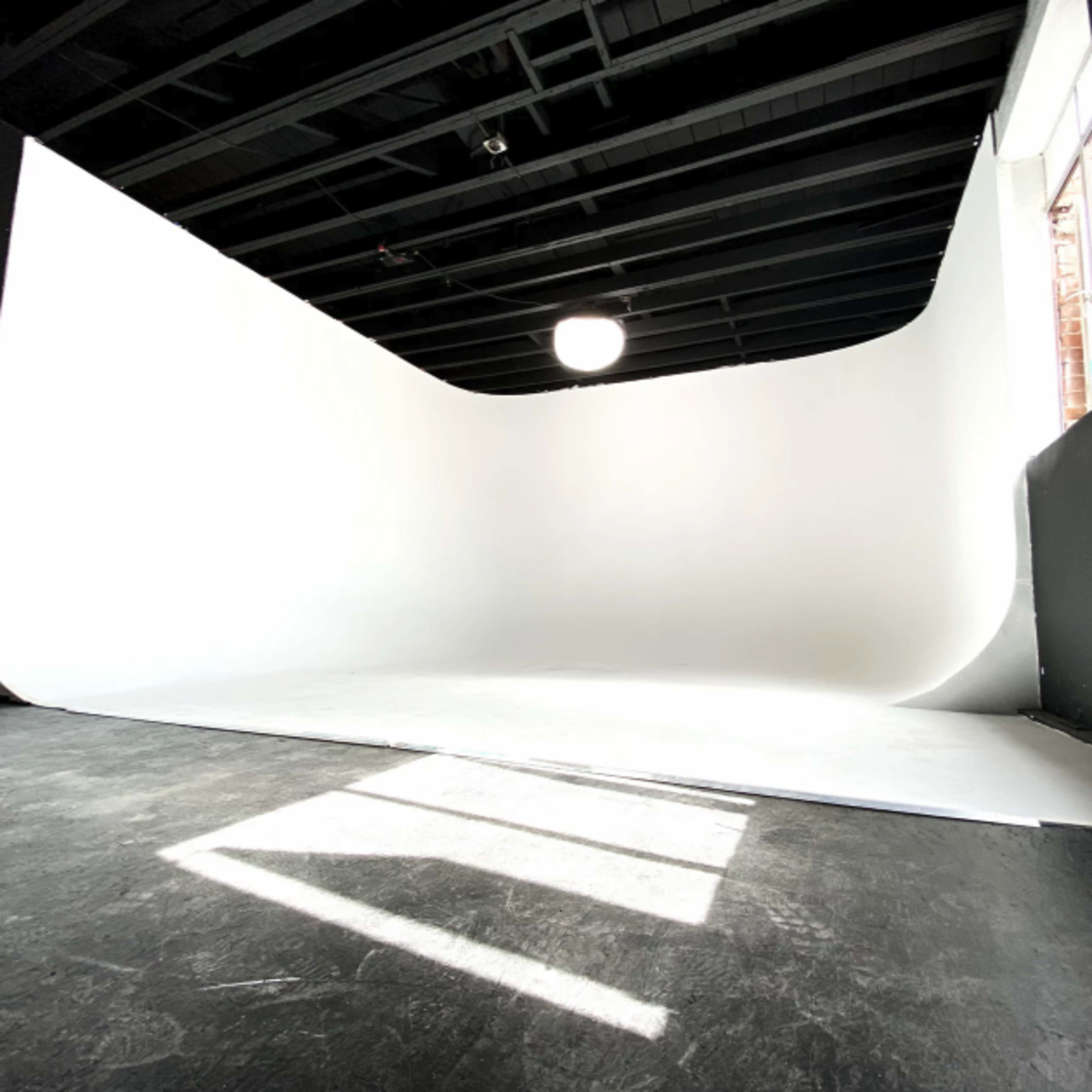 A photography studio with a seamless white backdrop and a softbox light source.