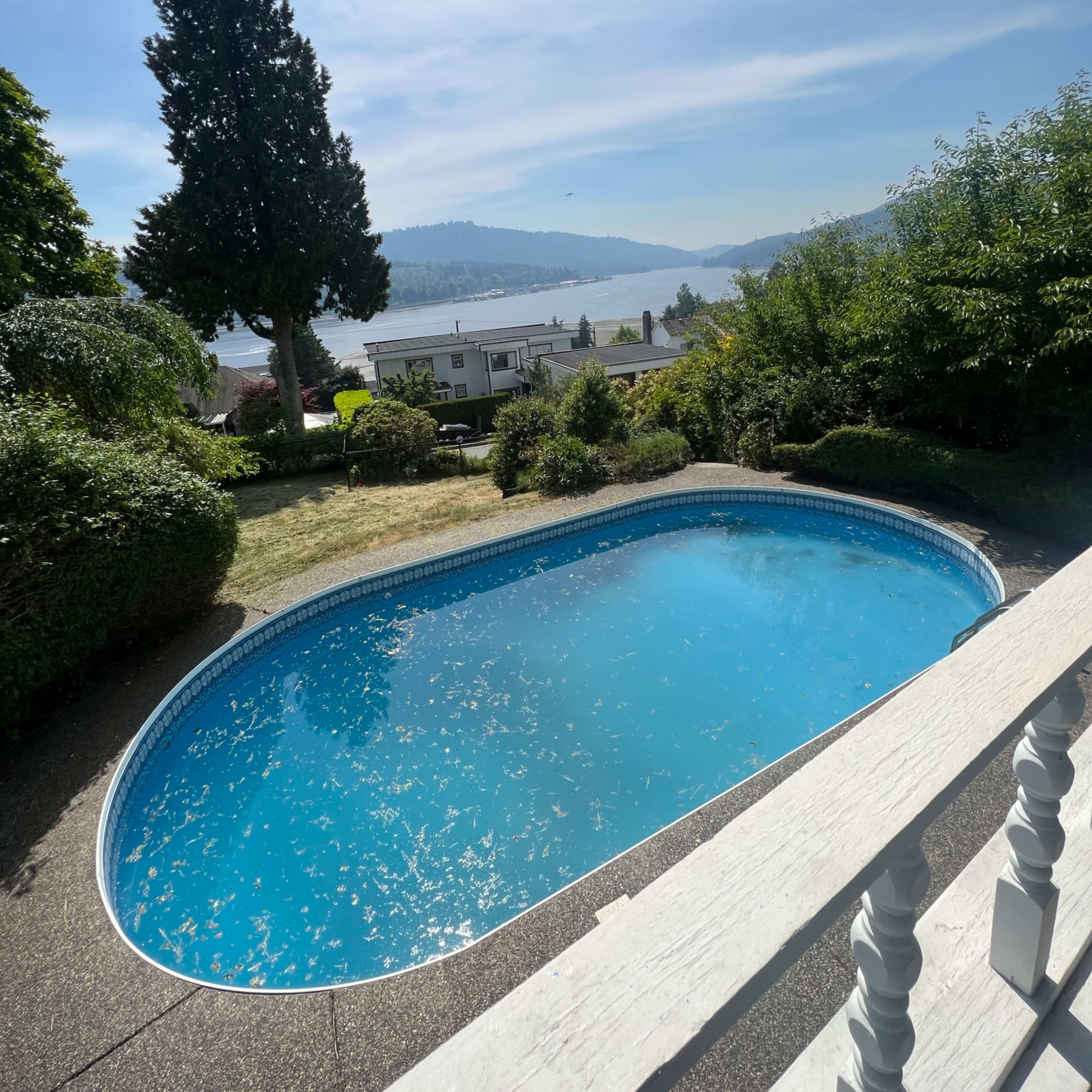 A blue swimming pool surrounded by greenery and a view of a lake and hills in the background.