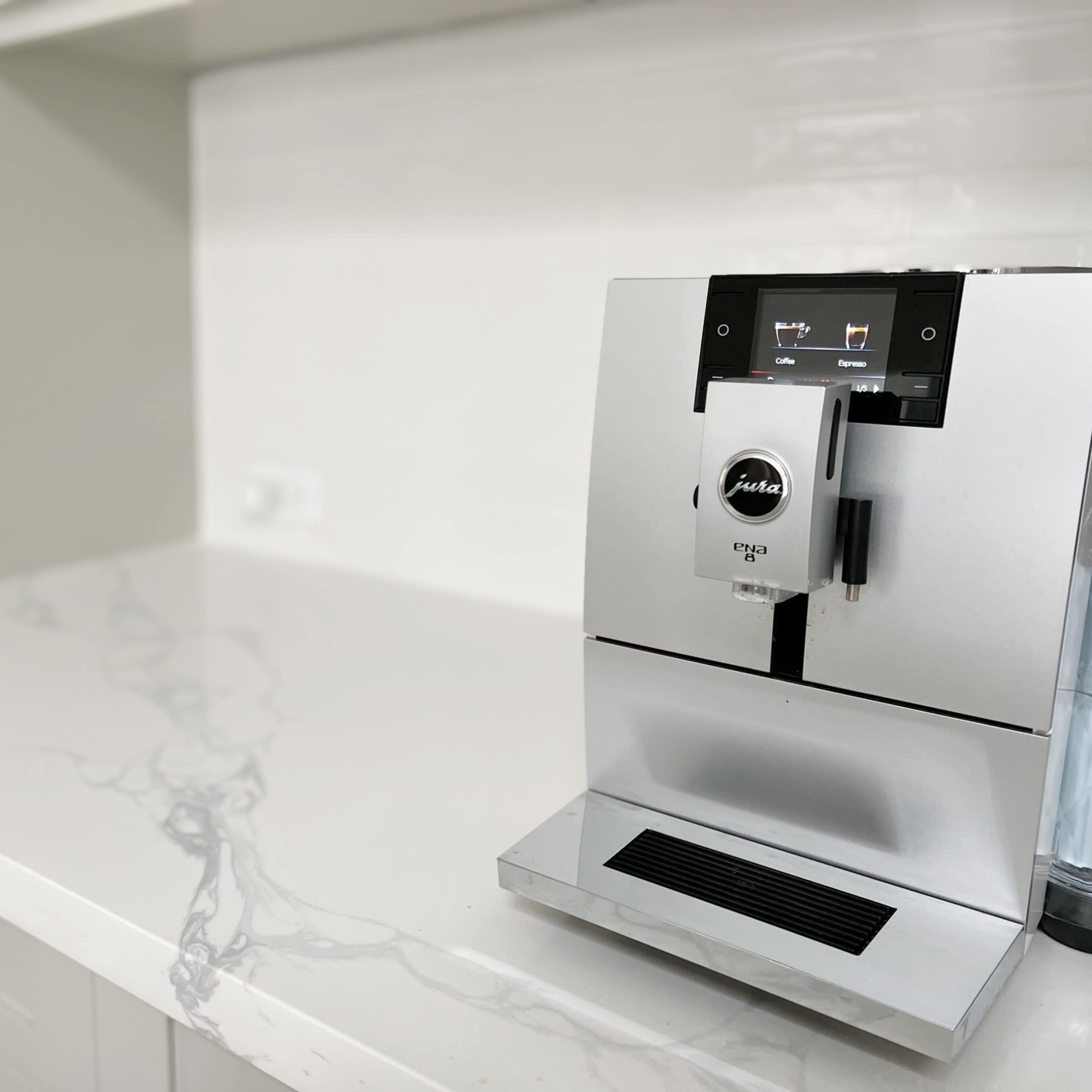 A silver coffee machine is positioned on a white marbled countertop in a modern kitchen.