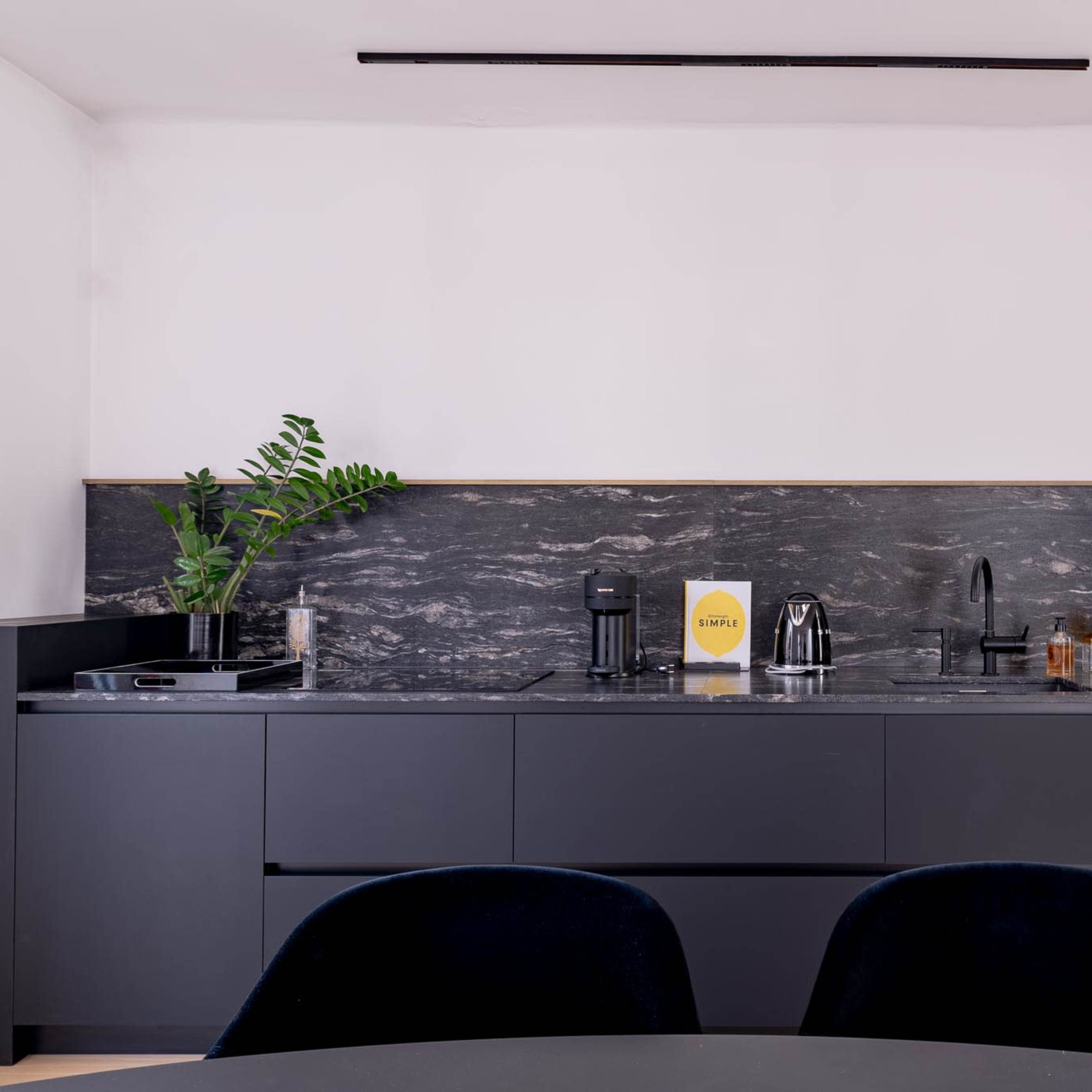 A modern kitchen with a dark cabinetry design, a sleek countertop, and minimal appliances.