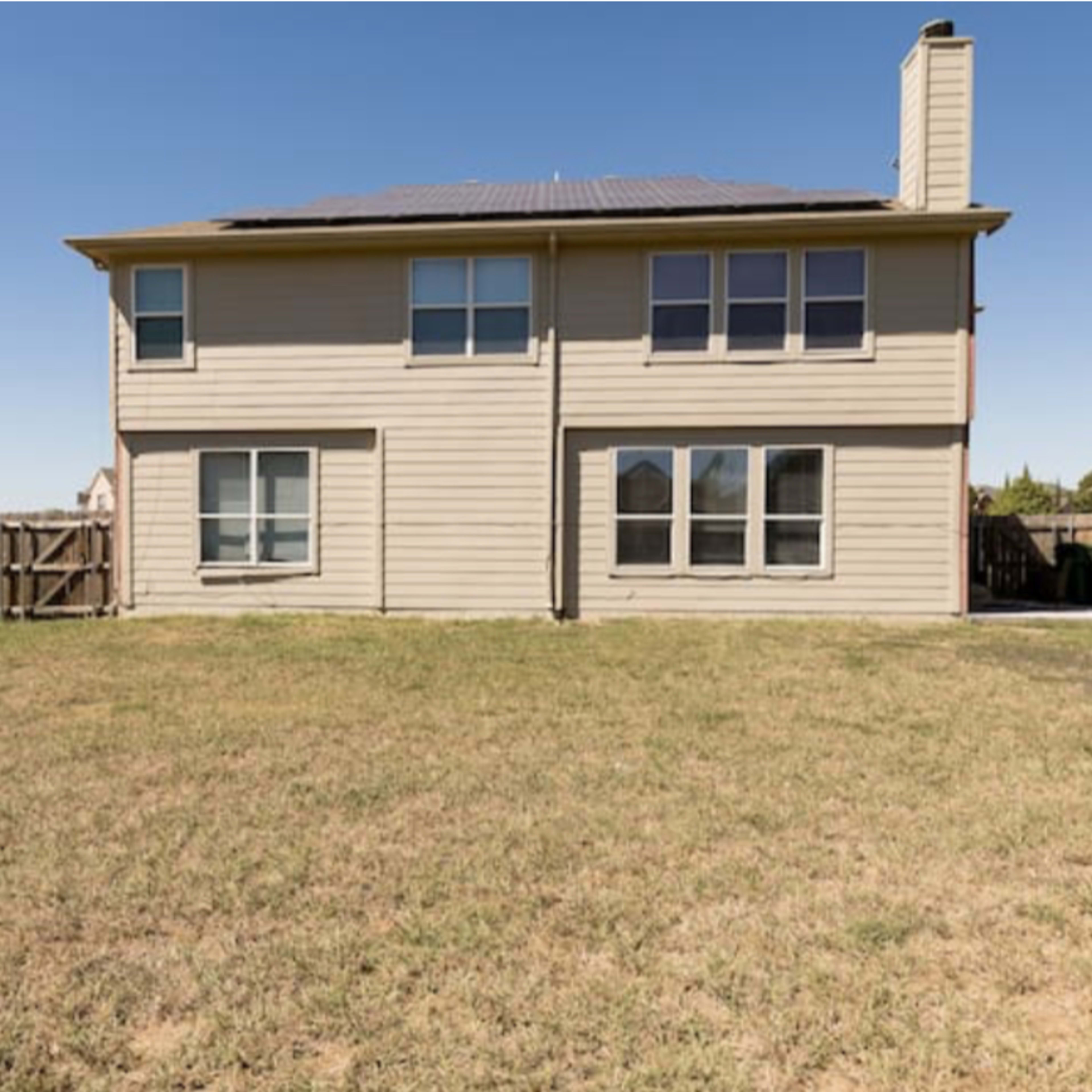 A two-story house with a fenced backyard and solar panels on the roof.