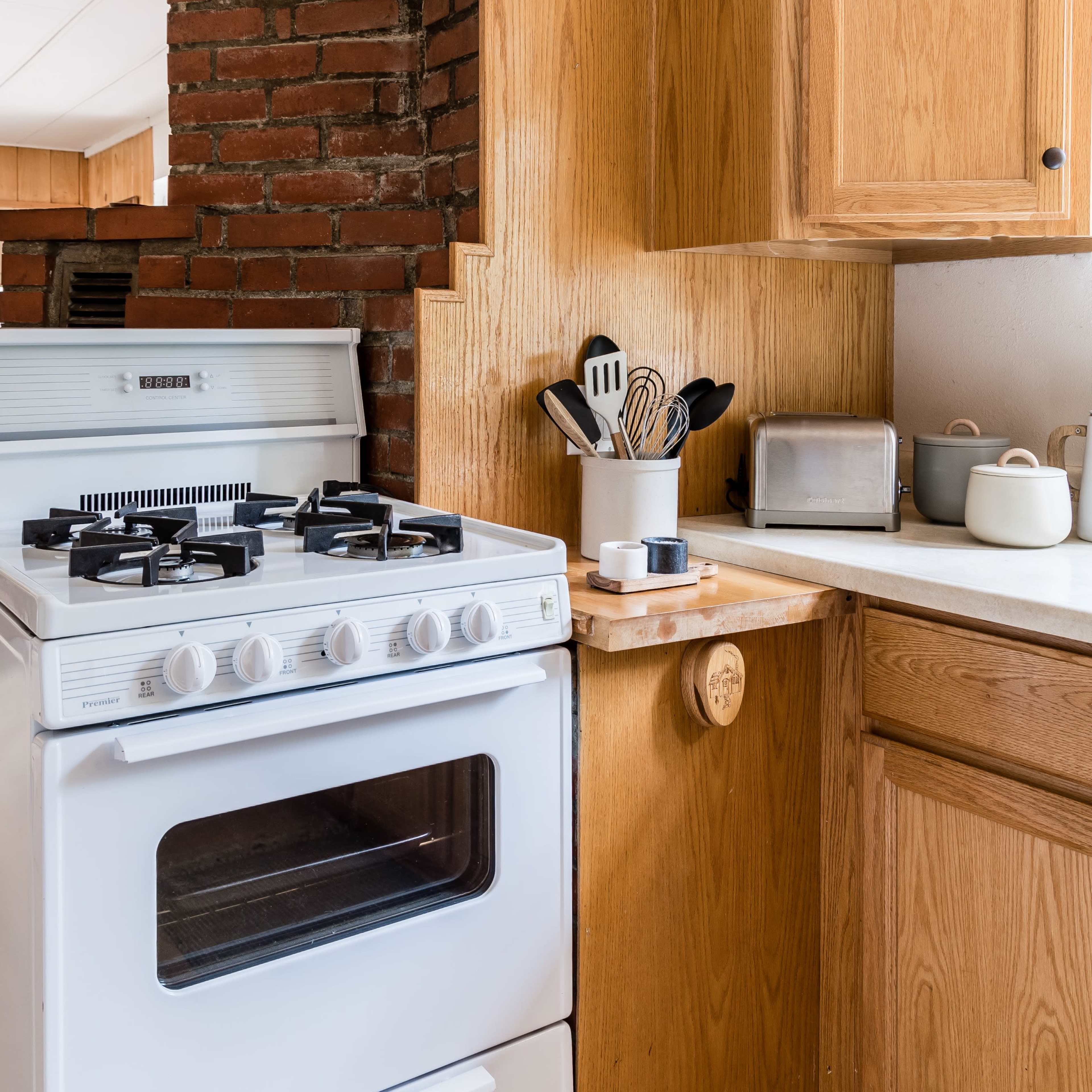 A kitchen with a white gas stove, wooden cabinets, and a brick wall in the background.