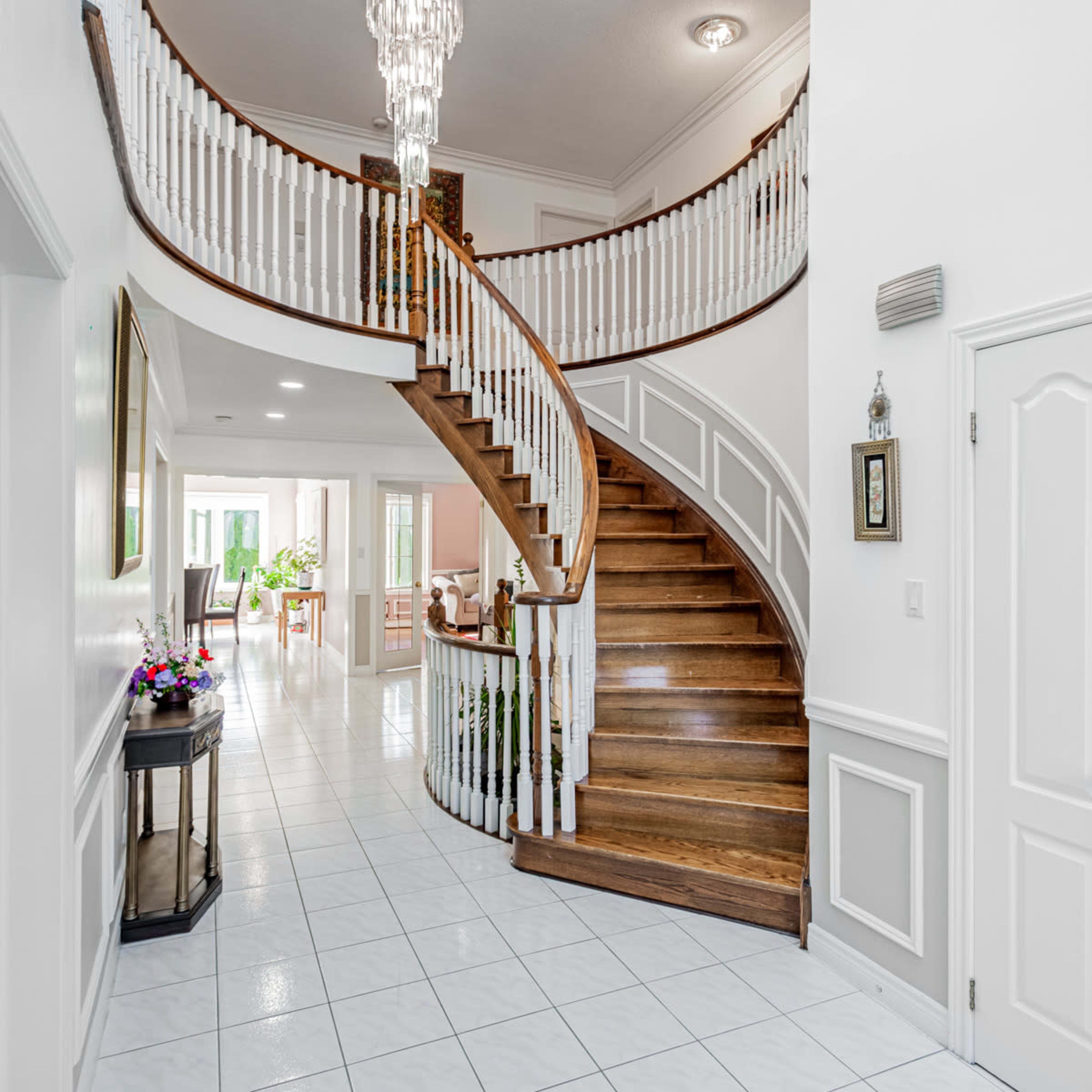 A bright foyer with a sweeping staircase, white walls, and tiled flooring leading to an open living area.