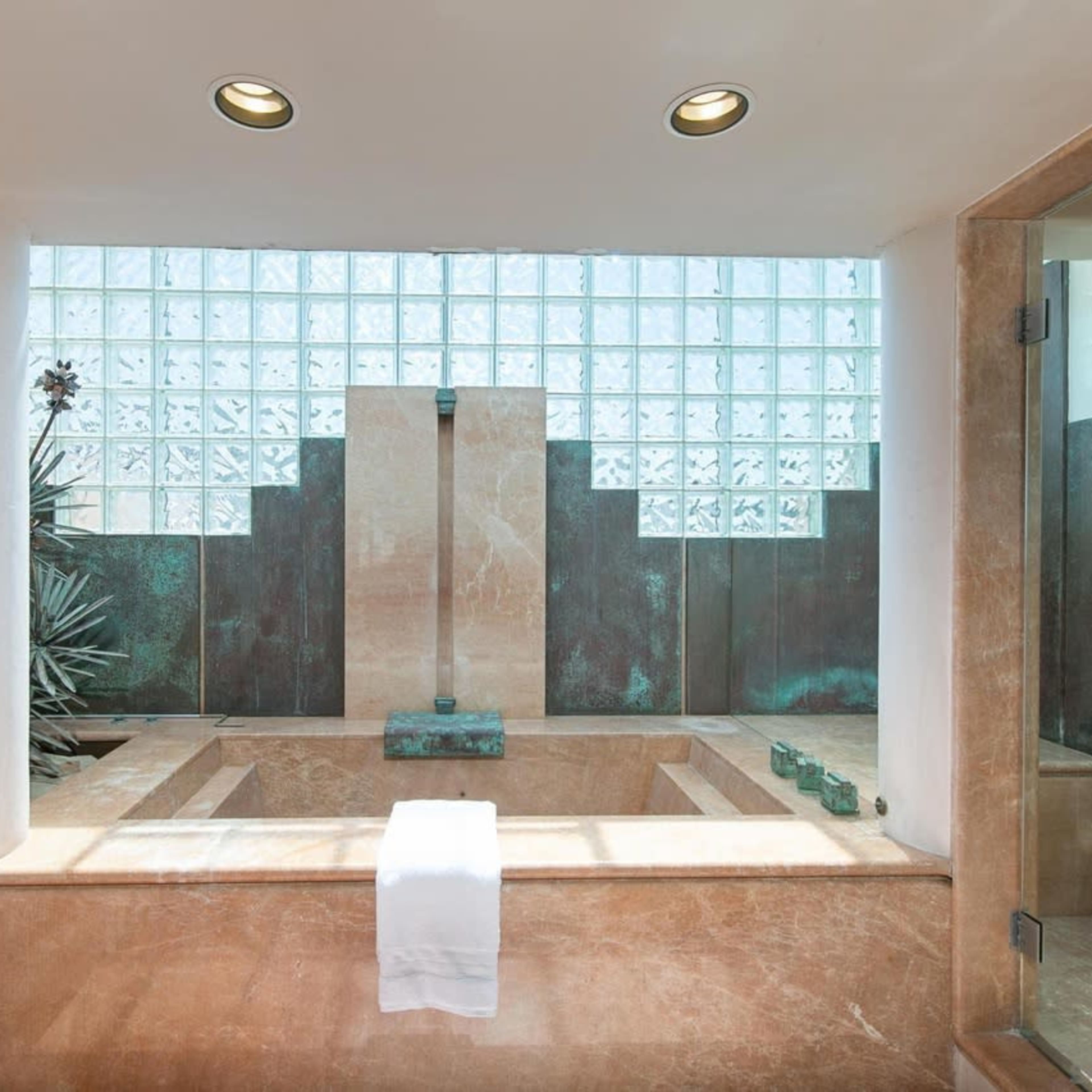 A modern bathroom featuring a stone bath, glass block windows, and a large shower area.