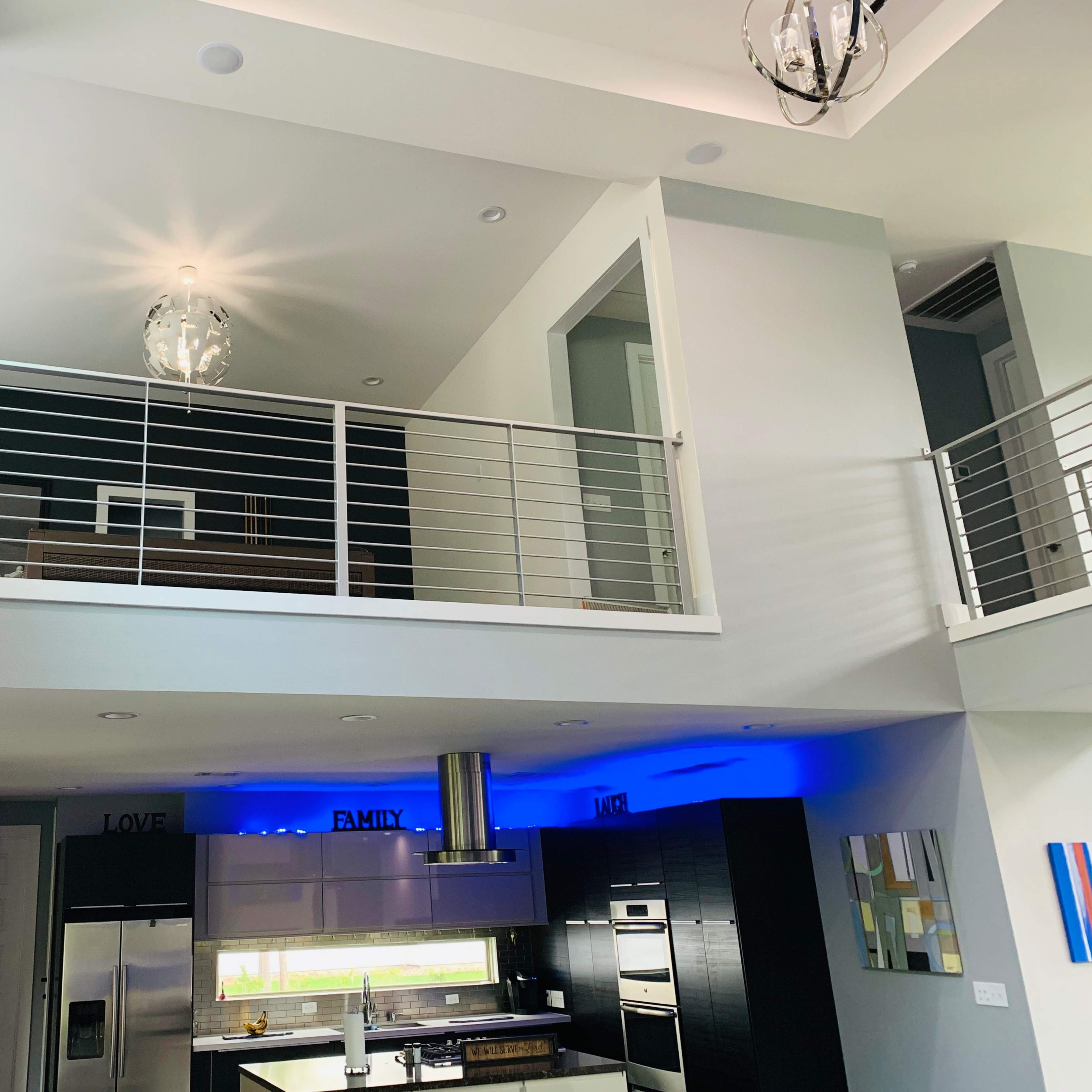 A modern interior space with an open floor plan, featuring a kitchen below and a balcony above, illuminated by natural light and a pendant fixture.
