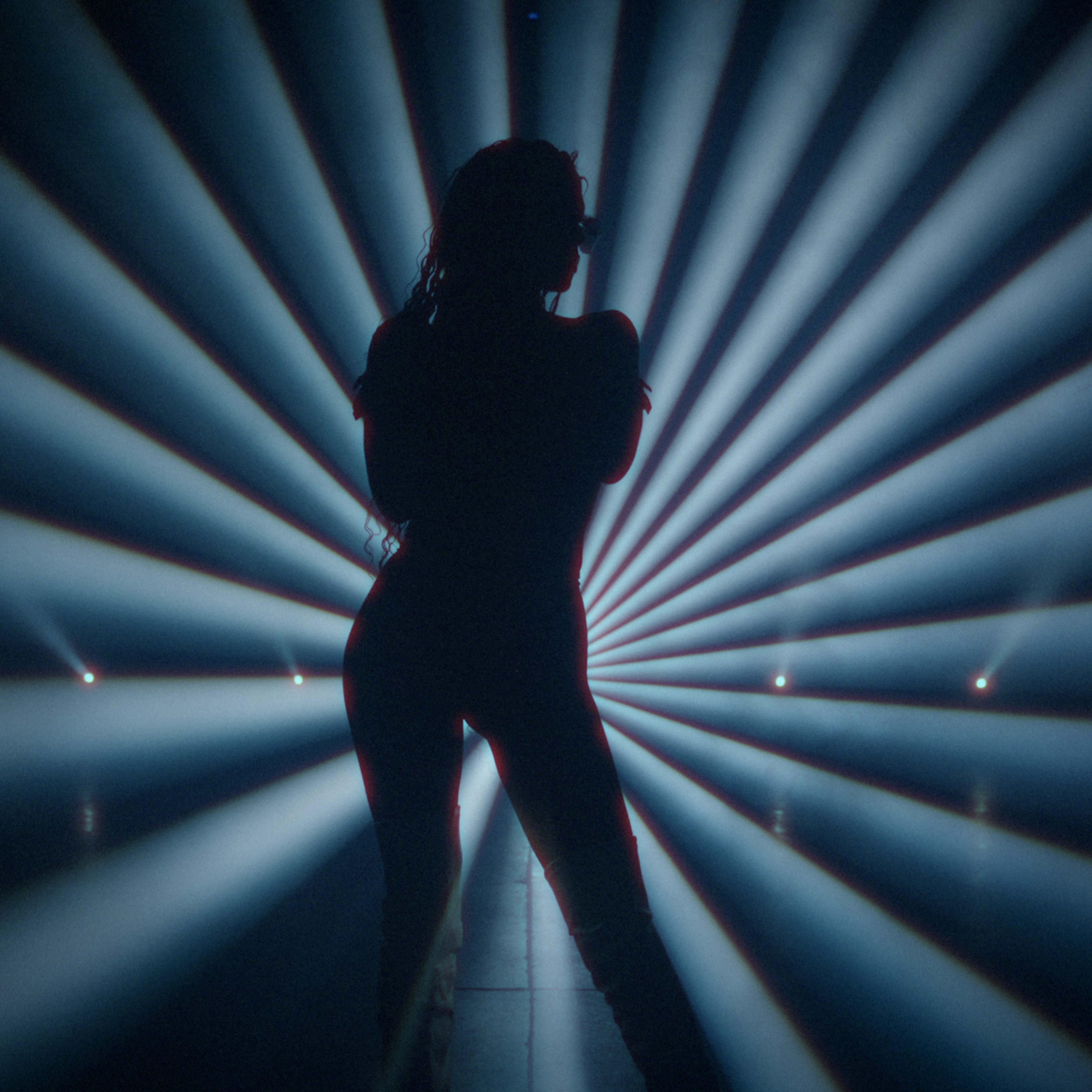A silhouetted figure stands against a backdrop of rays of light emanating from the center of the scene.