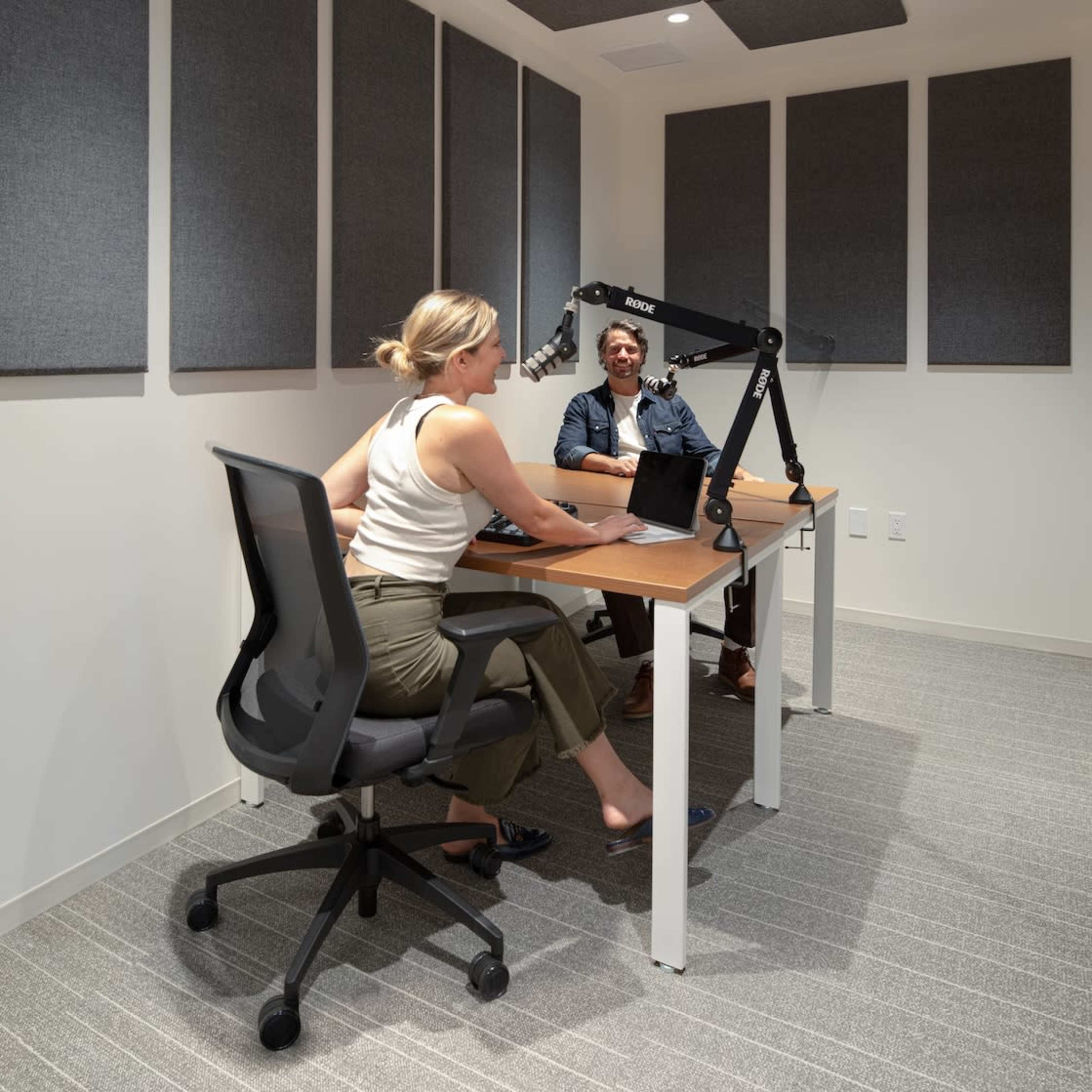 Two individuals are seated in a soundproofed meeting room with acoustic panels, one working on a laptop while the other engages in conversation.
