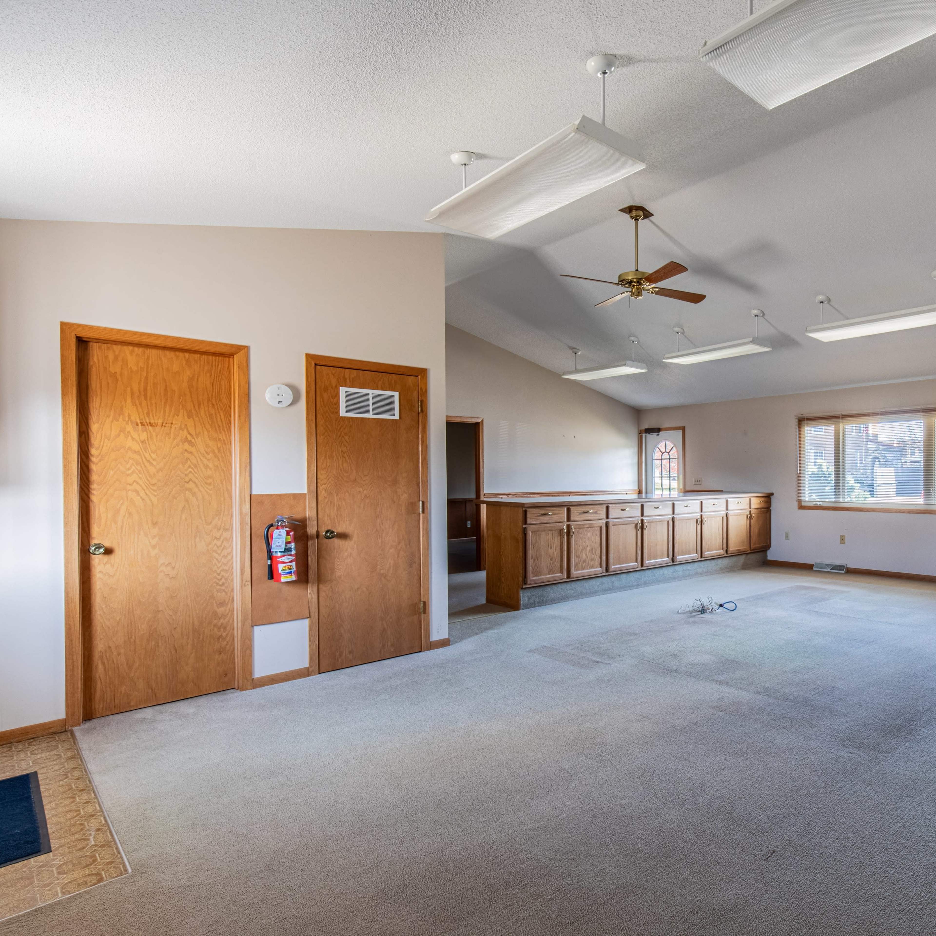 A spacious room with beige carpet, a ceiling fan, and two wooden doors.