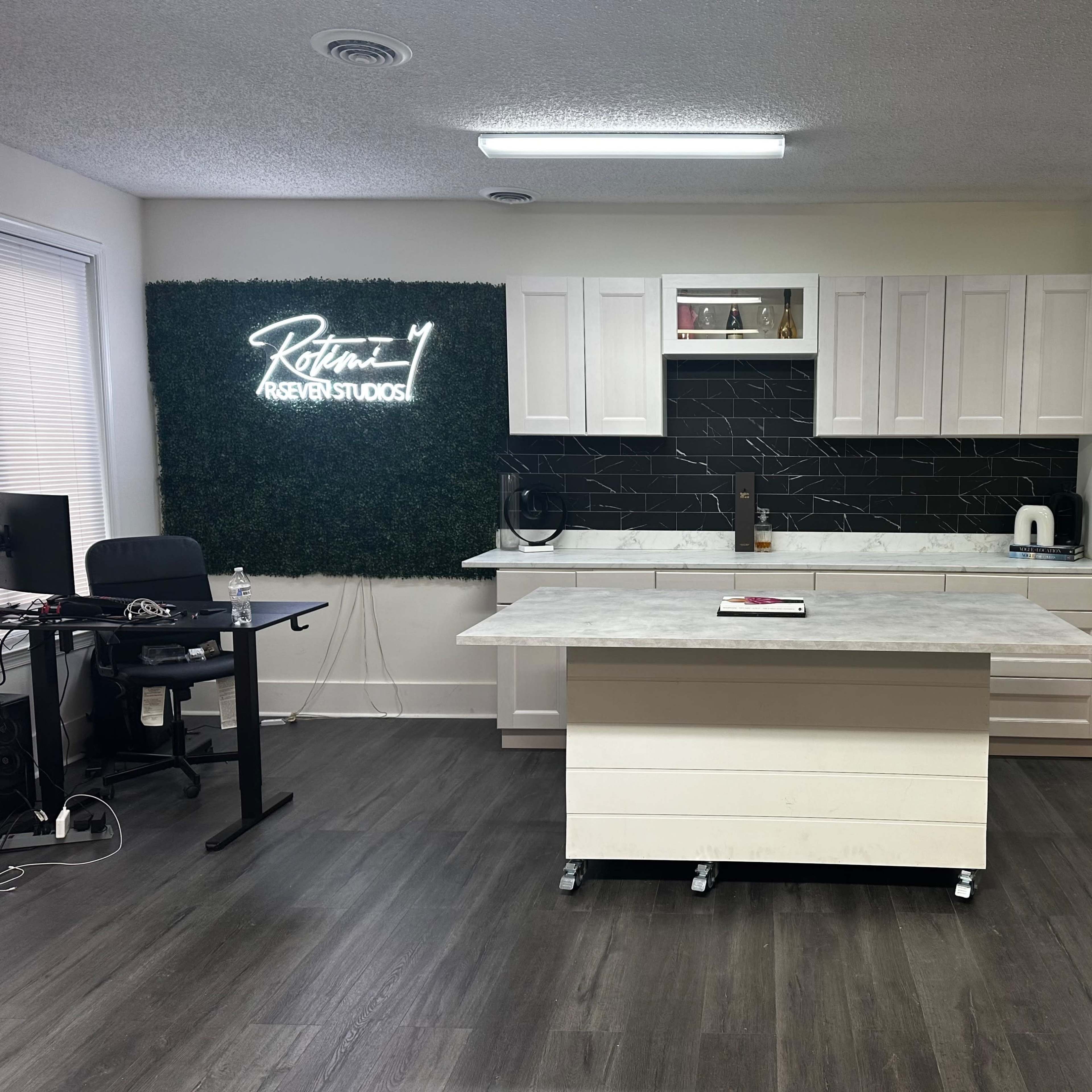 A modern kitchen space featuring white cabinetry, a large island with a marble countertop, and a green wall with illuminated text.