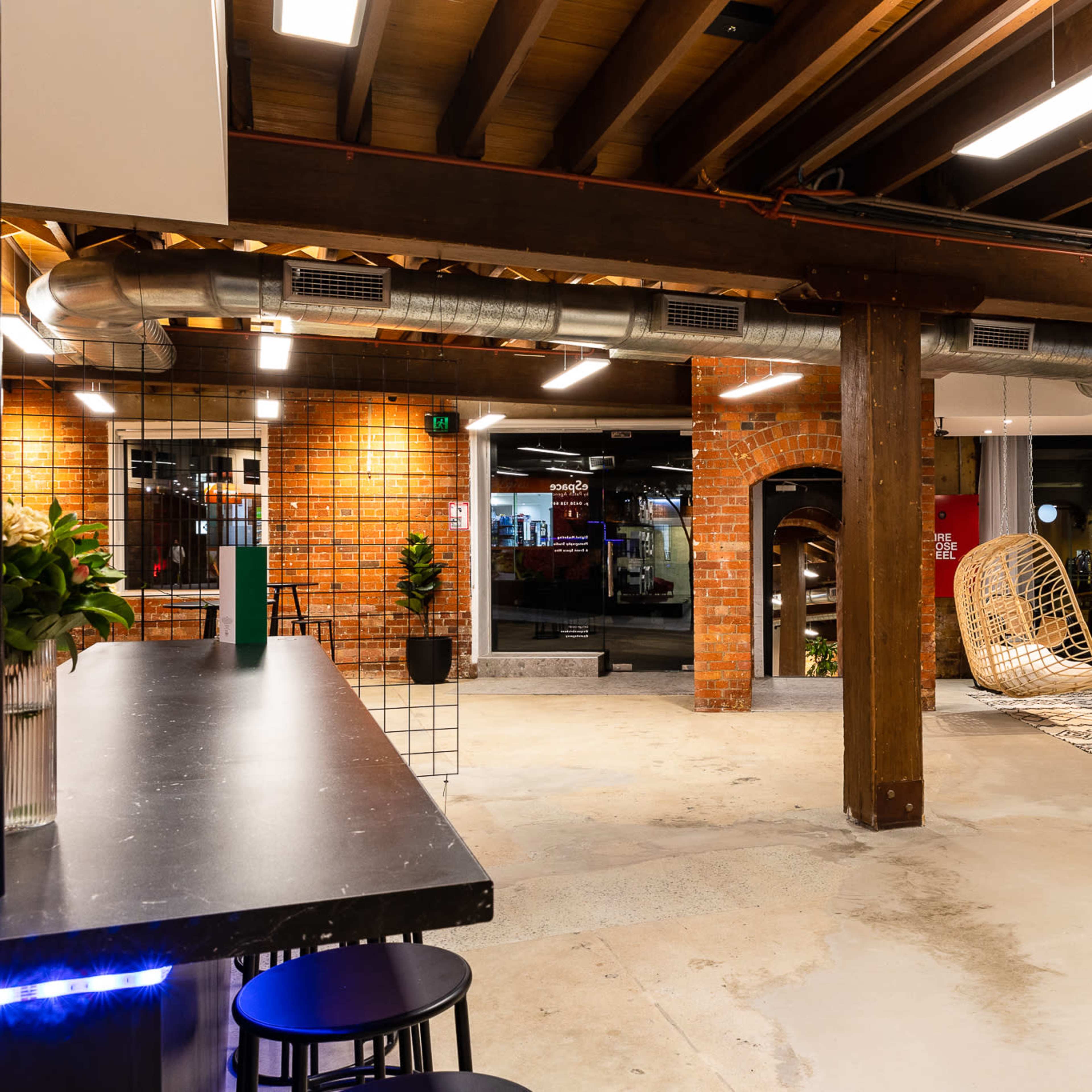 A spacious, modern interior featuring exposed wooden beams, a seating area with a yellow couch, and a bar counter with black stools.