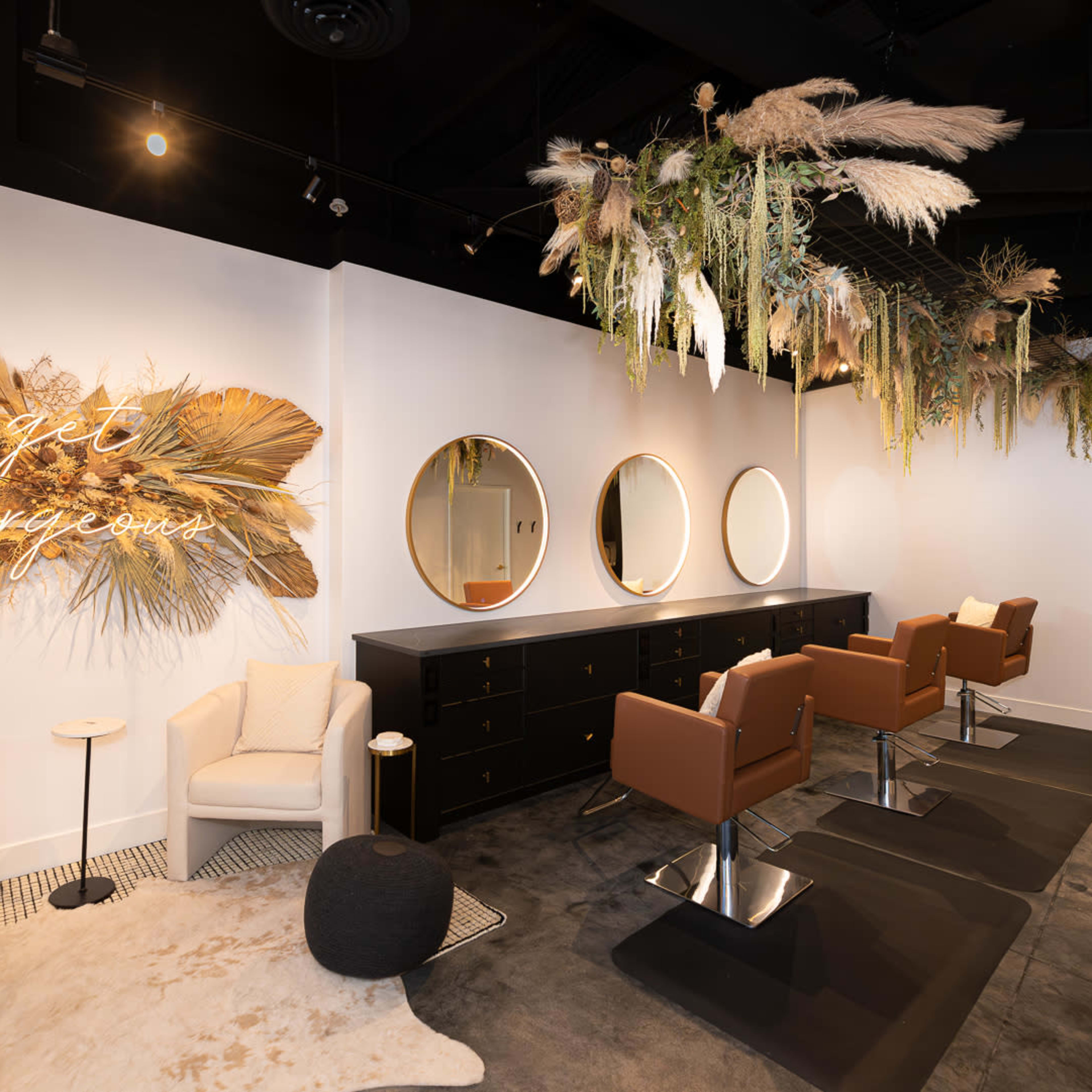 A modern beauty salon with a stylish interior featuring round mirrors, brown chairs, and greenery decor hanging from the ceiling.