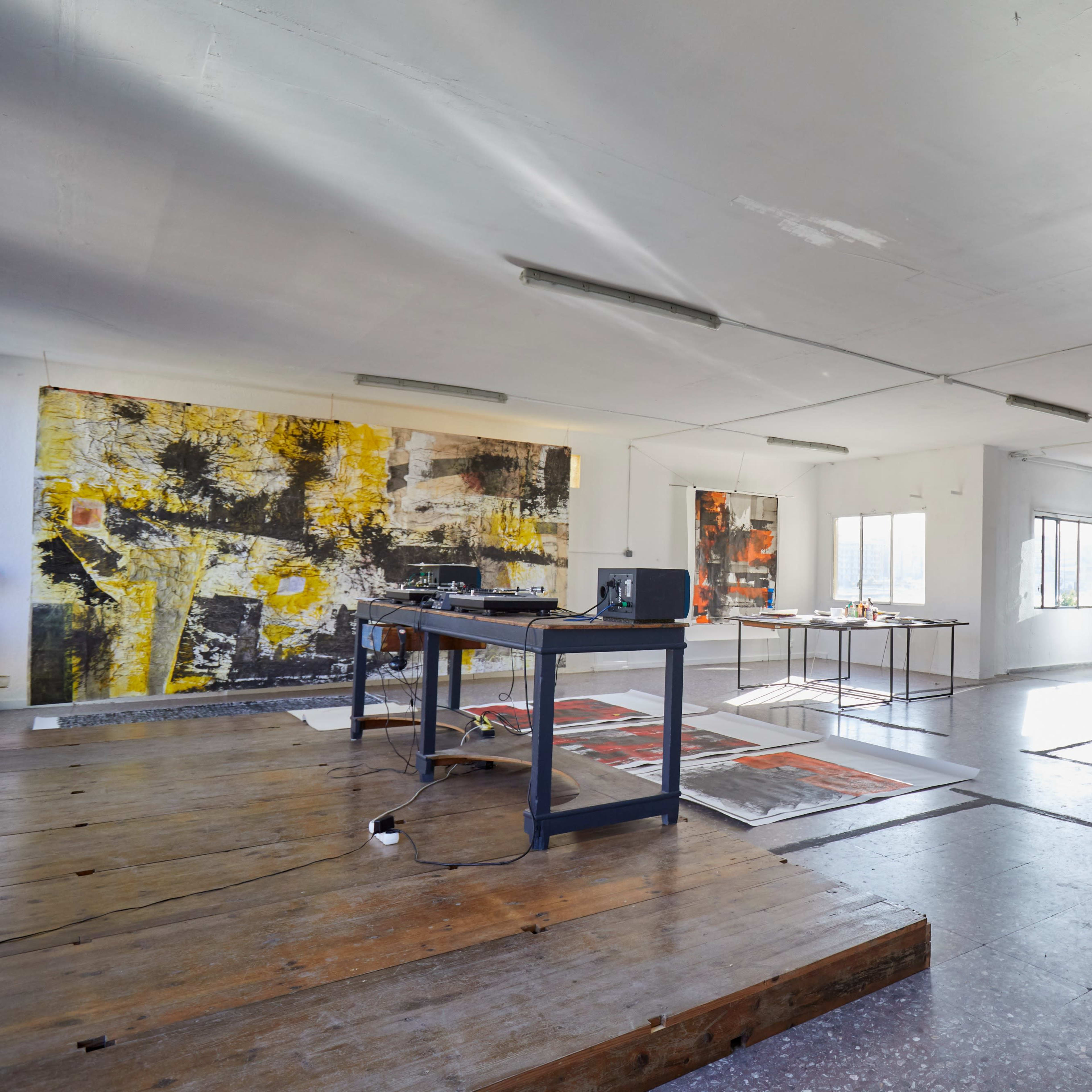 An open, spacious studio area featuring large abstract paintings on the walls, a wooden table with a projector, and modern furniture including a dining table and chairs.