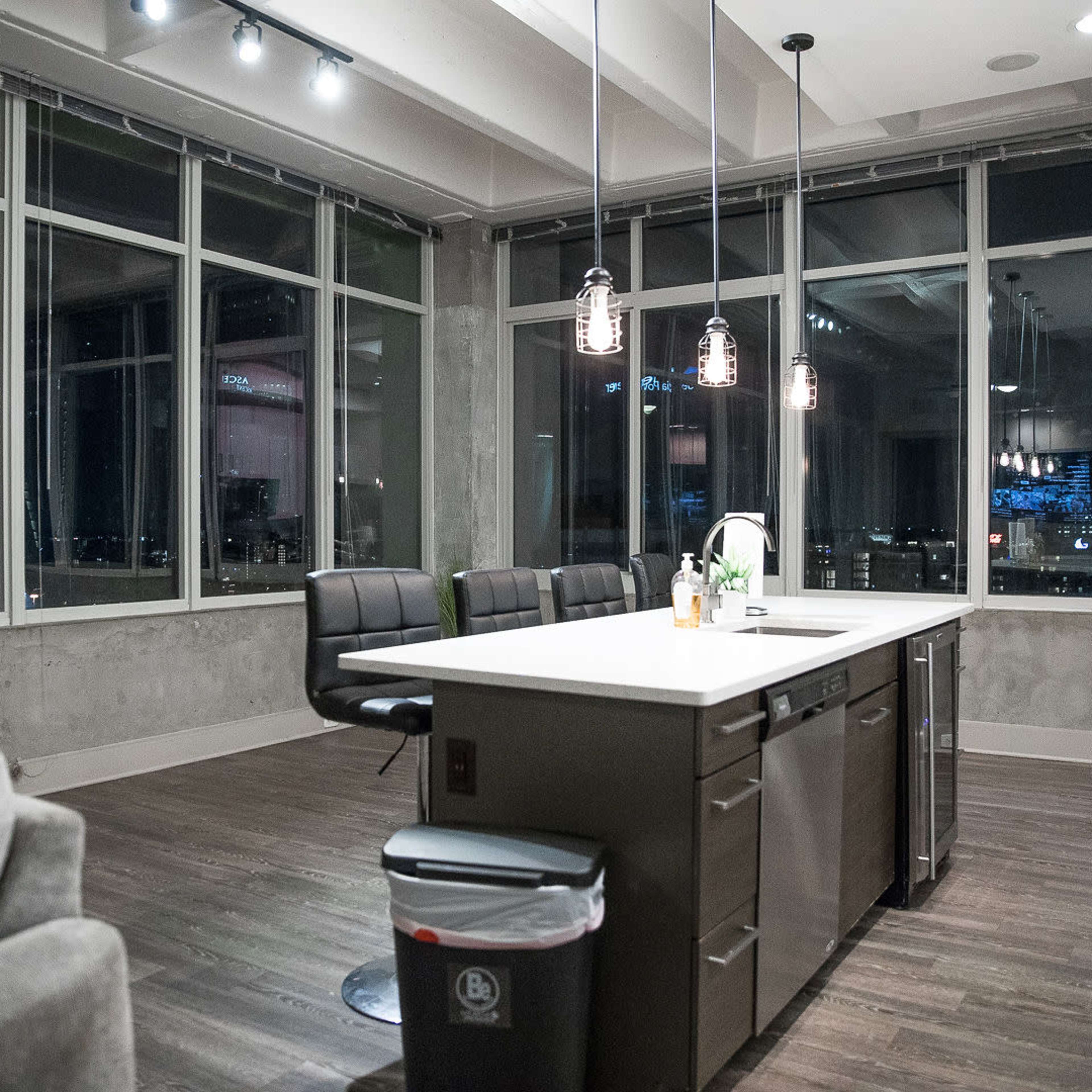 A modern kitchen with large windows offers a view of a city skyline, featuring an island counter and seating area.