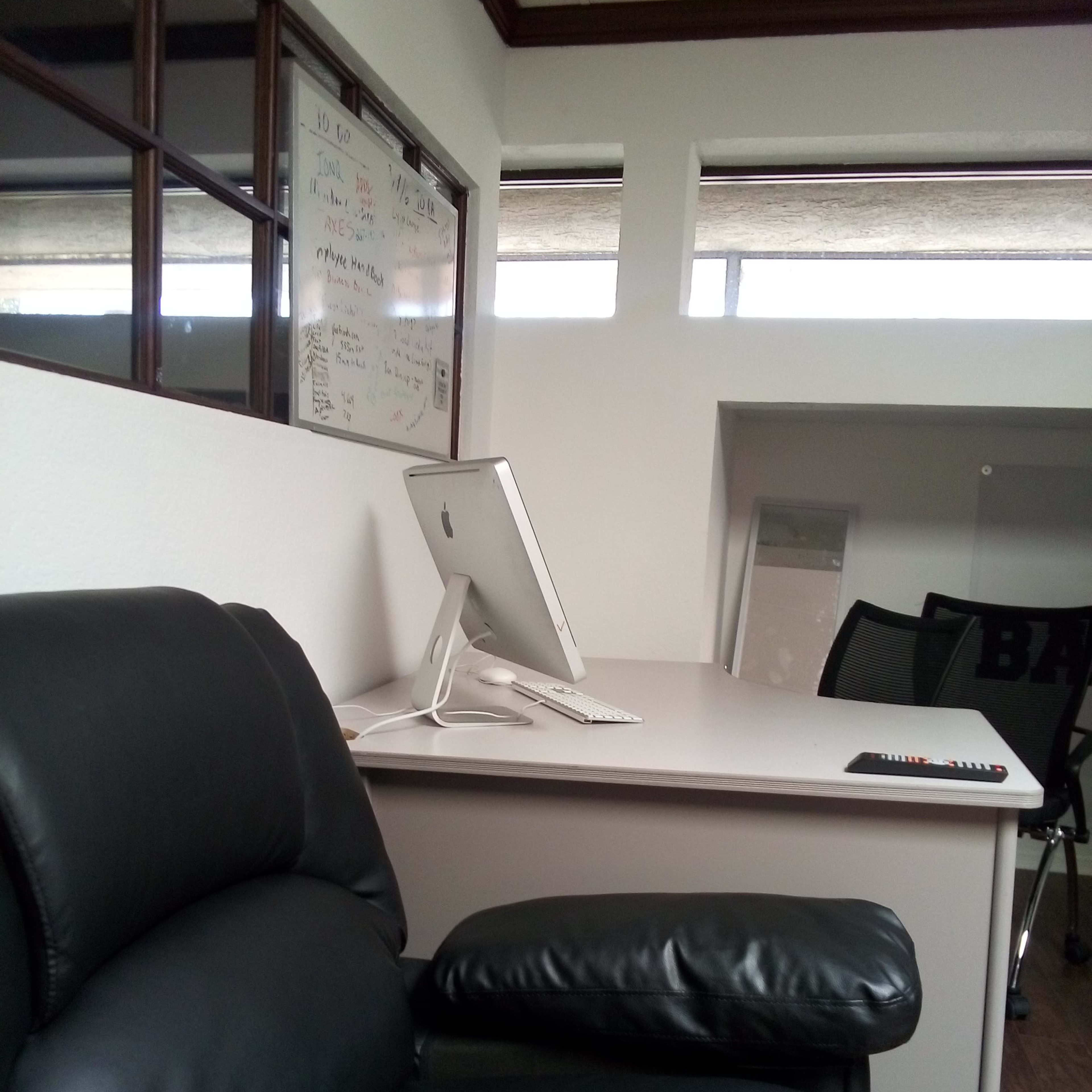A modern office space featuring a black leather chair beside a white desk with a computer monitor and a remote control.