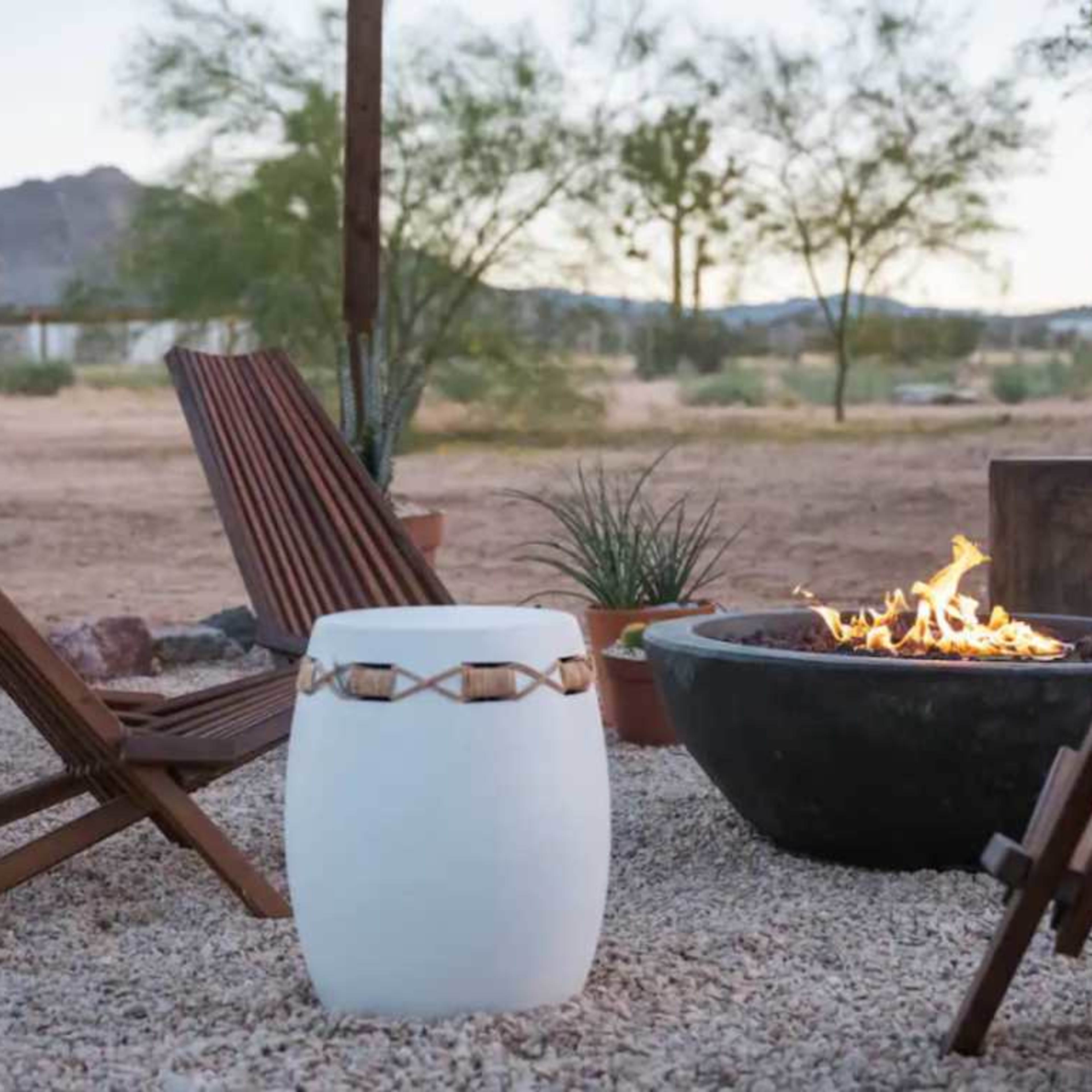 A fire pit surrounded by wooden chairs and potted plants in a desert landscape.