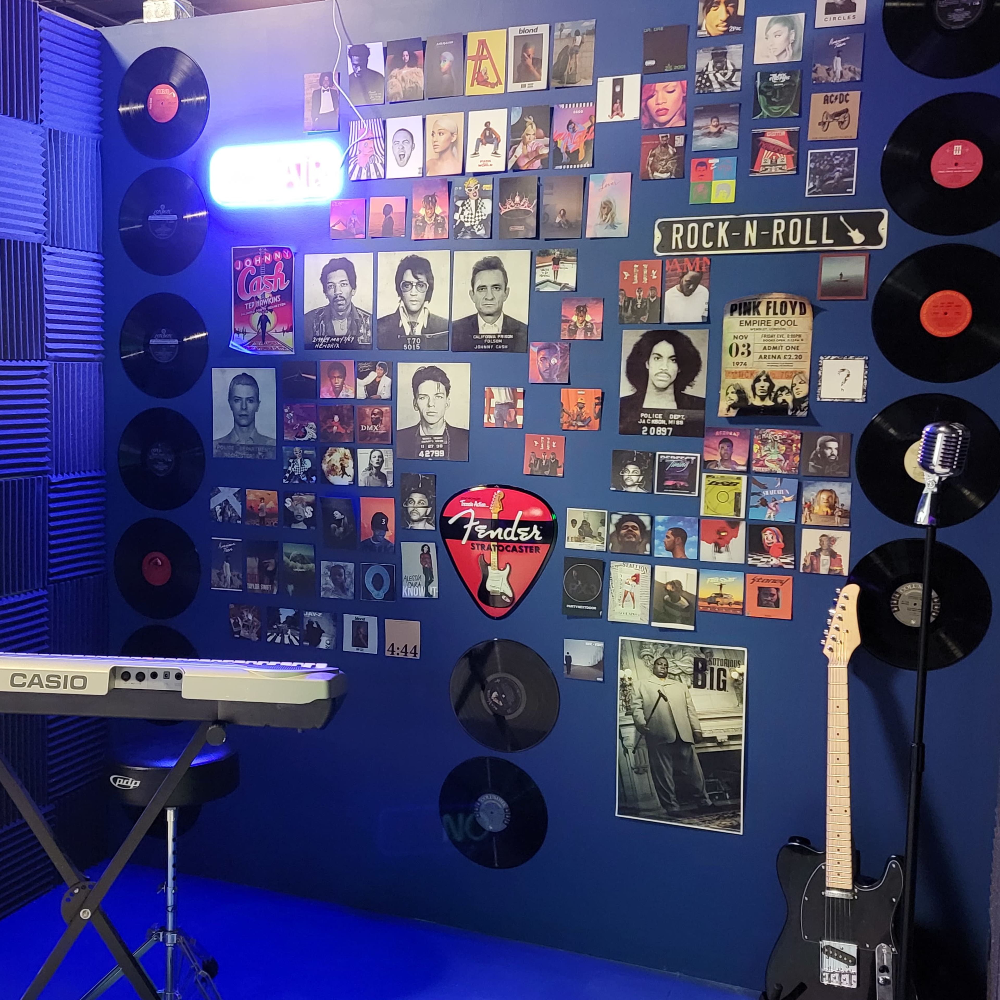A music-themed room with a keyboard on a stand, a microphone, and walls adorned with framed album covers and vinyl records.