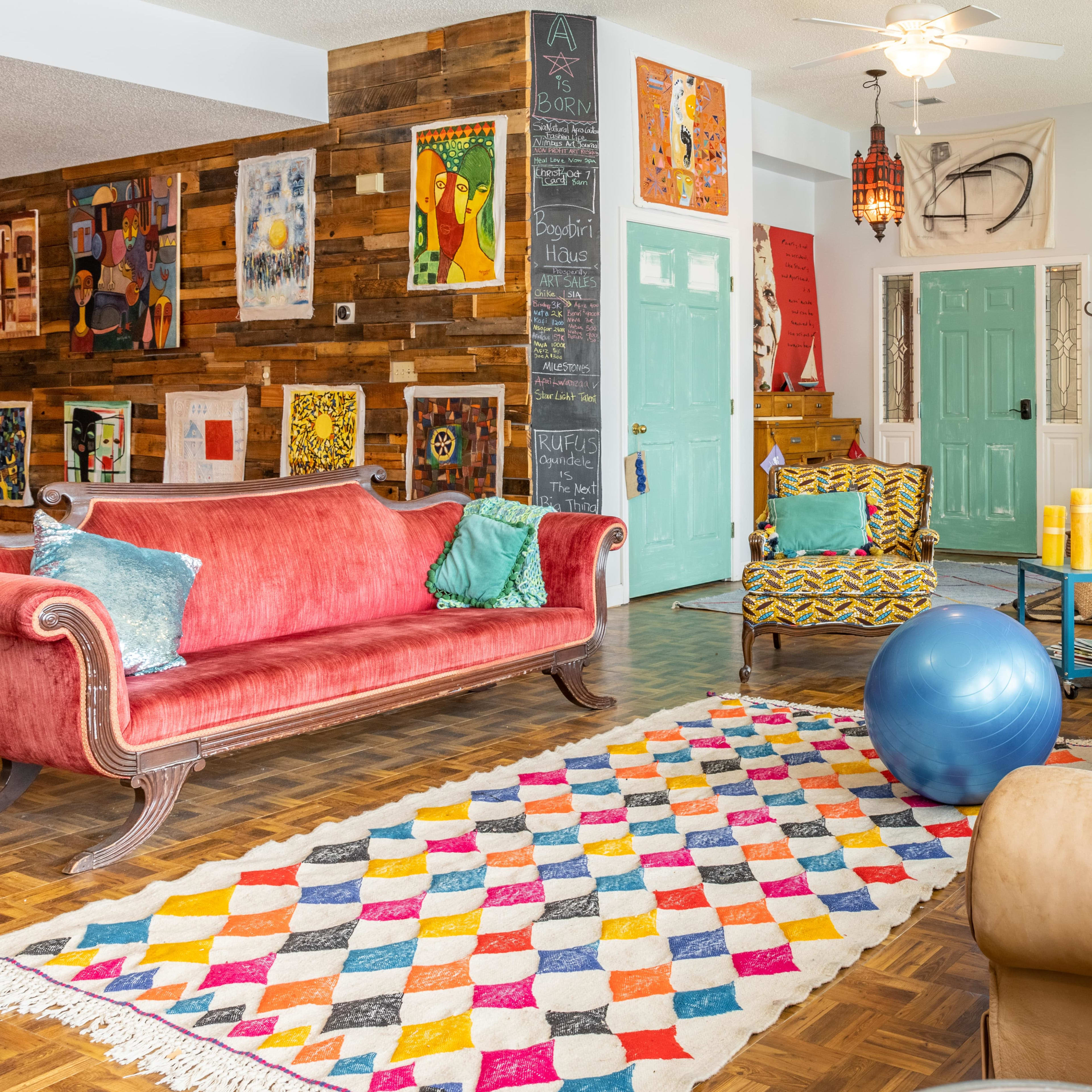 A bright, playful living room featuring a variety of seating options, colorful artwork on the walls, and a patterned rug on a wooden floor.