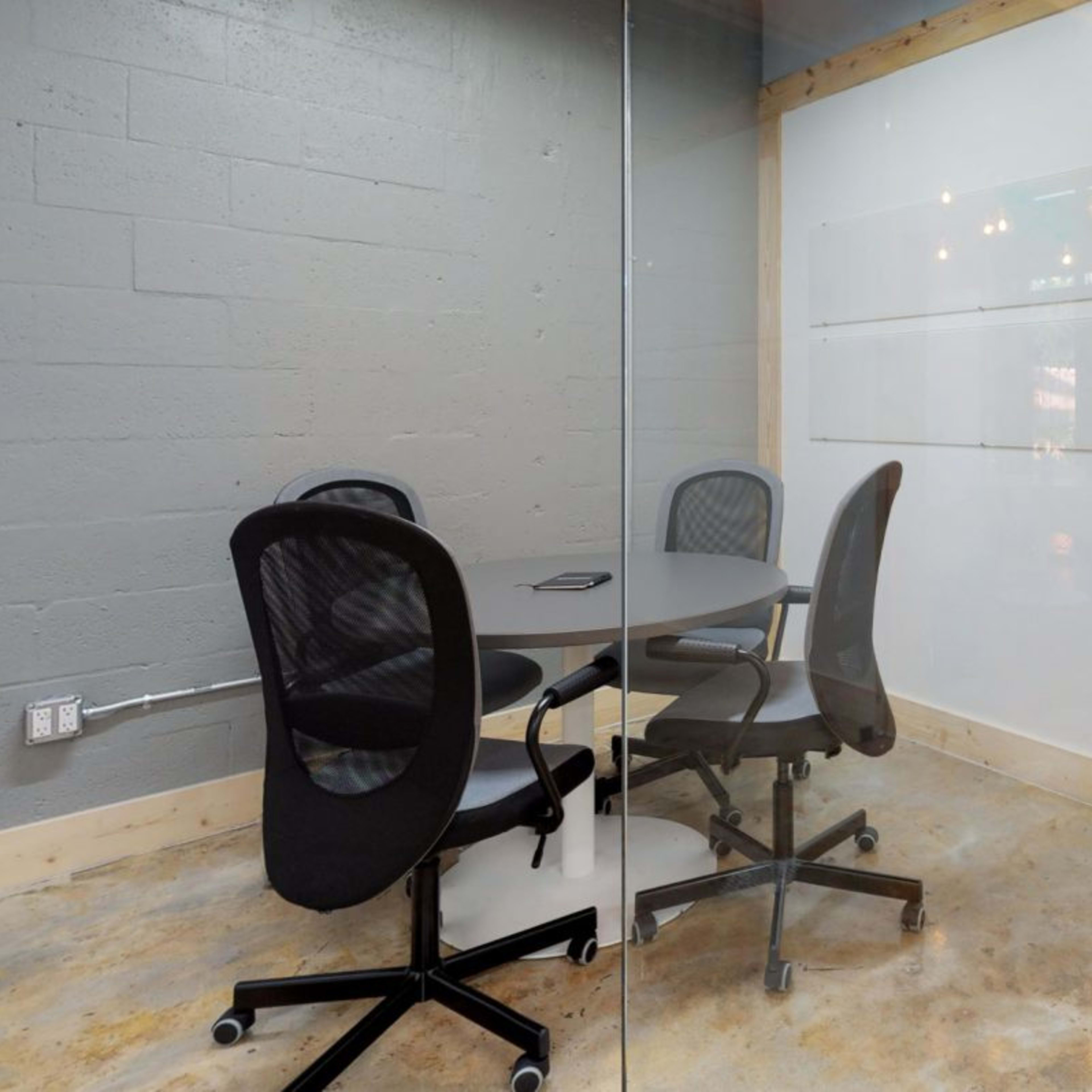 A conference room with a round table and four office chairs, enclosed by glass walls.