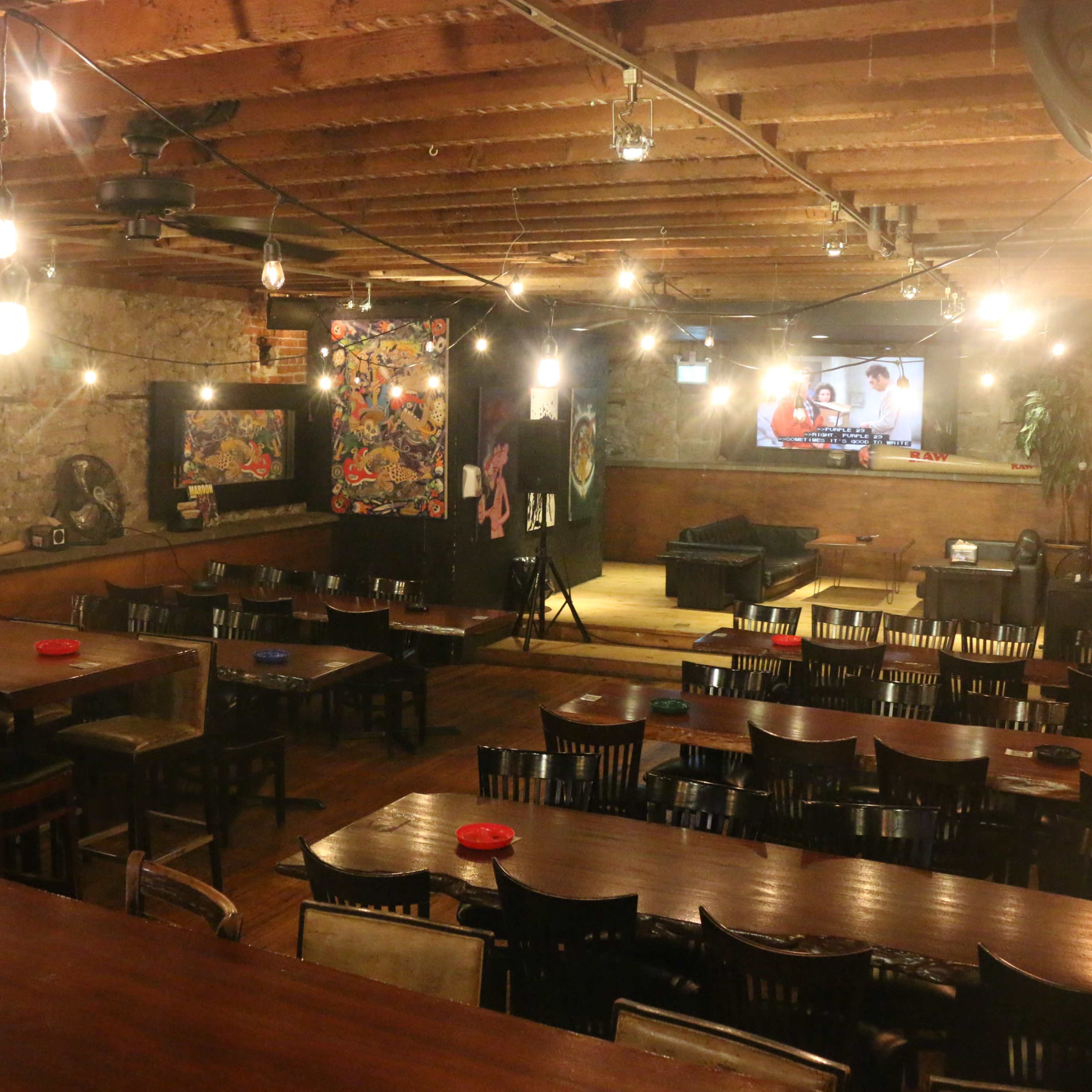 A dimly lit restaurant with wooden tables and chairs, exposed beams, and a large television on one wall.