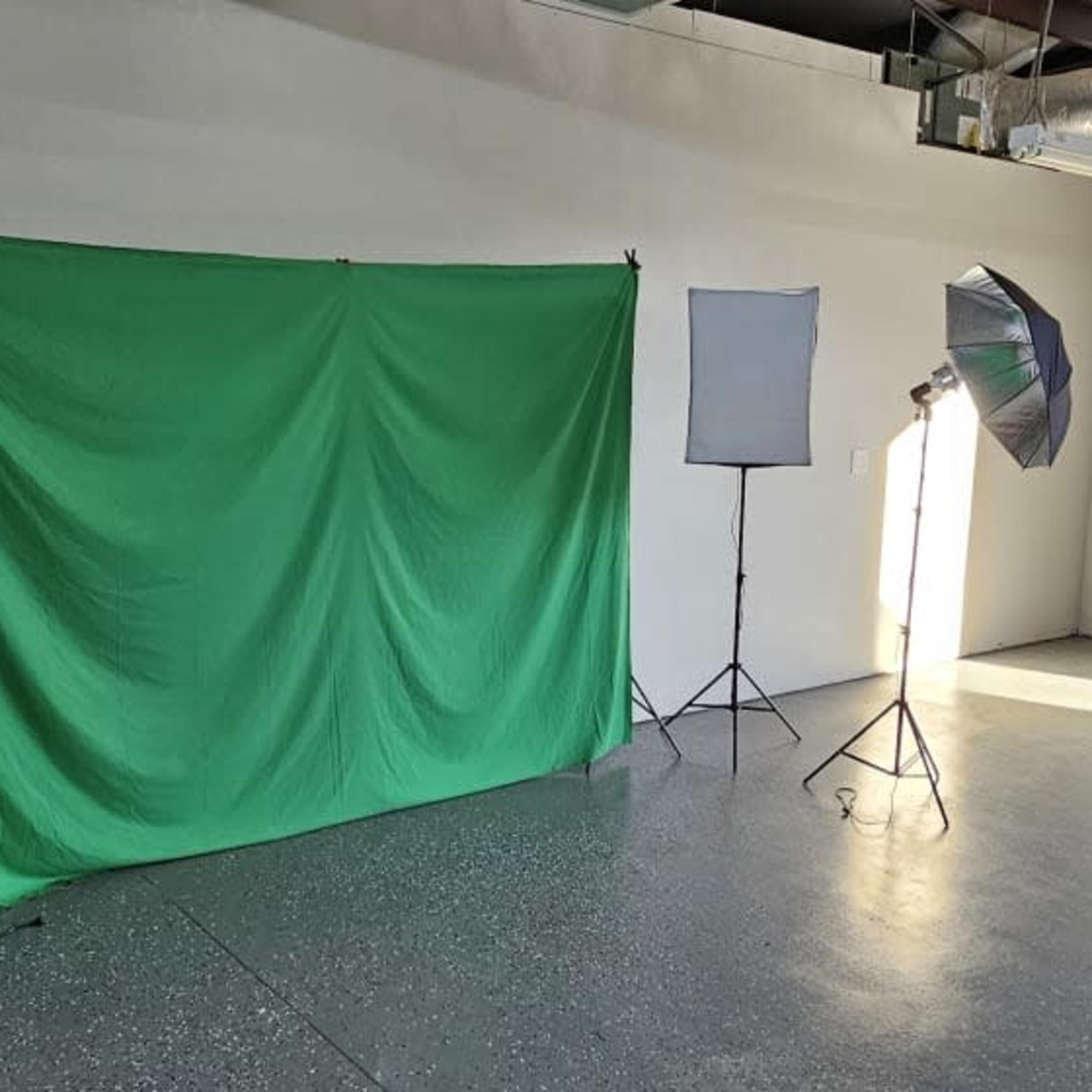A photography studio with a green backdrop and multiple lighting equipment set up in an empty room.