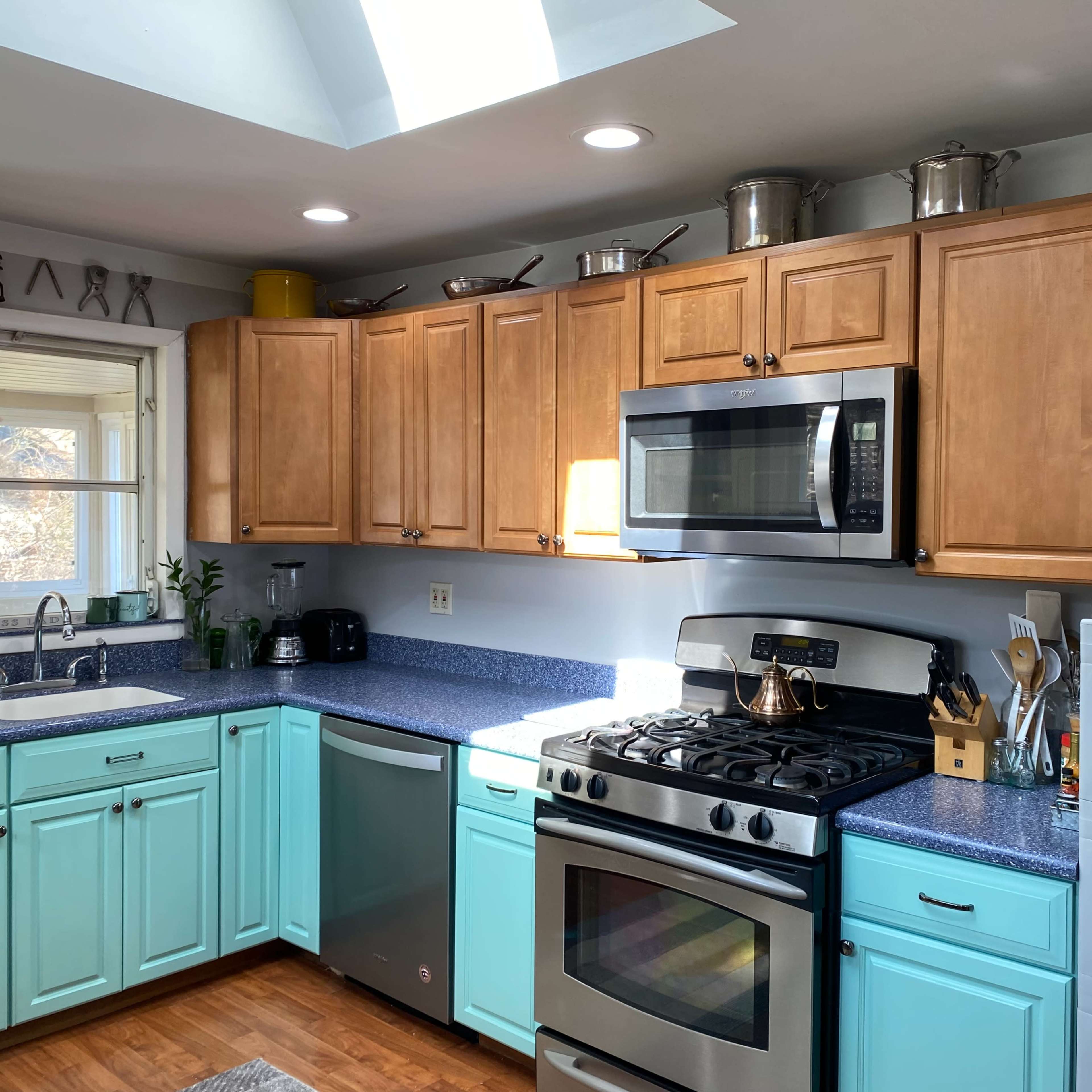 The kitchen features wooden cabinets, a blue countertop, and stainless steel appliances, with a skylight allowing natural light to enter.