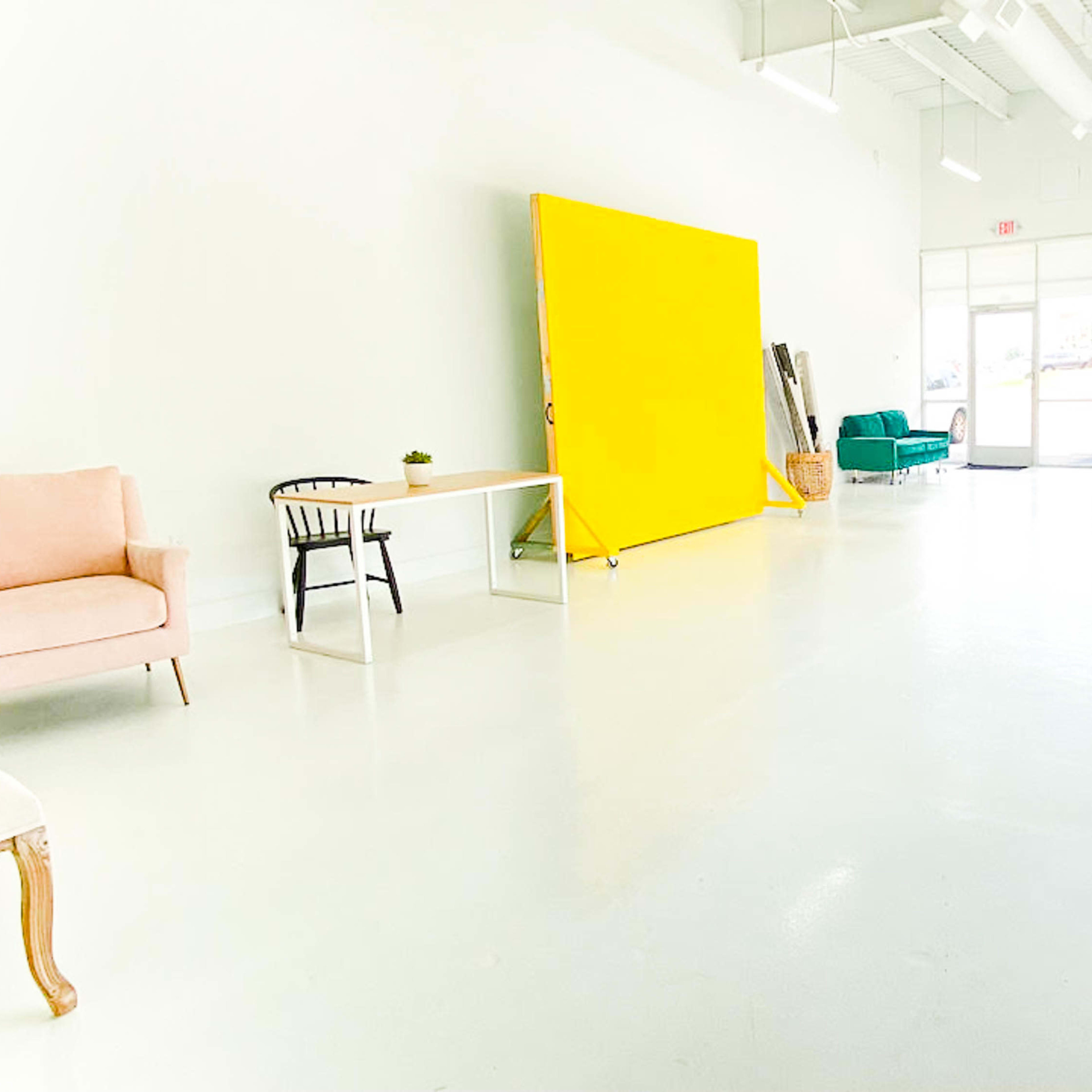 A spacious room with a bright yellow backdrop, various seating options including chairs and a couch, and large windows allowing natural light to fill the space.