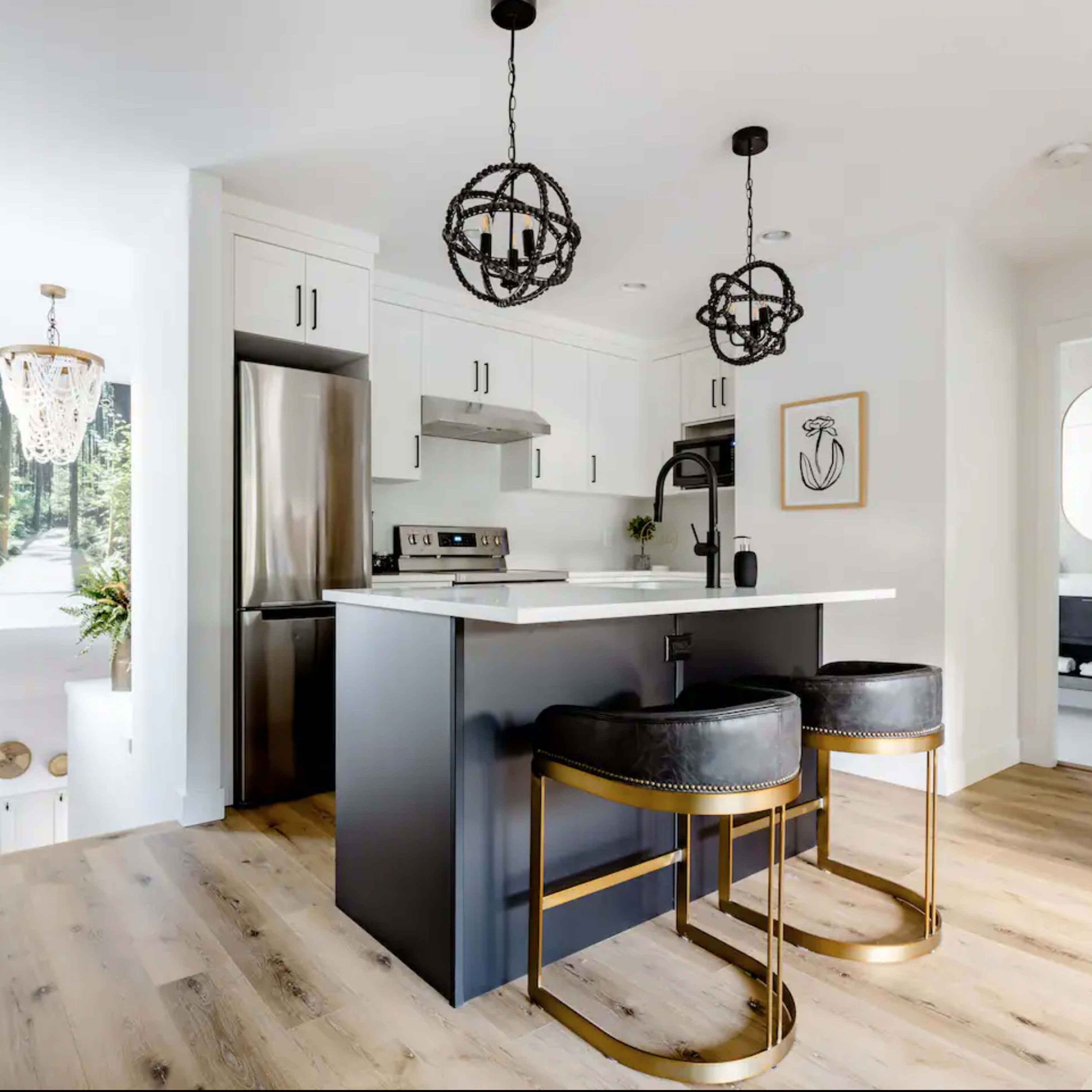 A modern kitchen with a central island, two black bar stools, and pendant lighting.