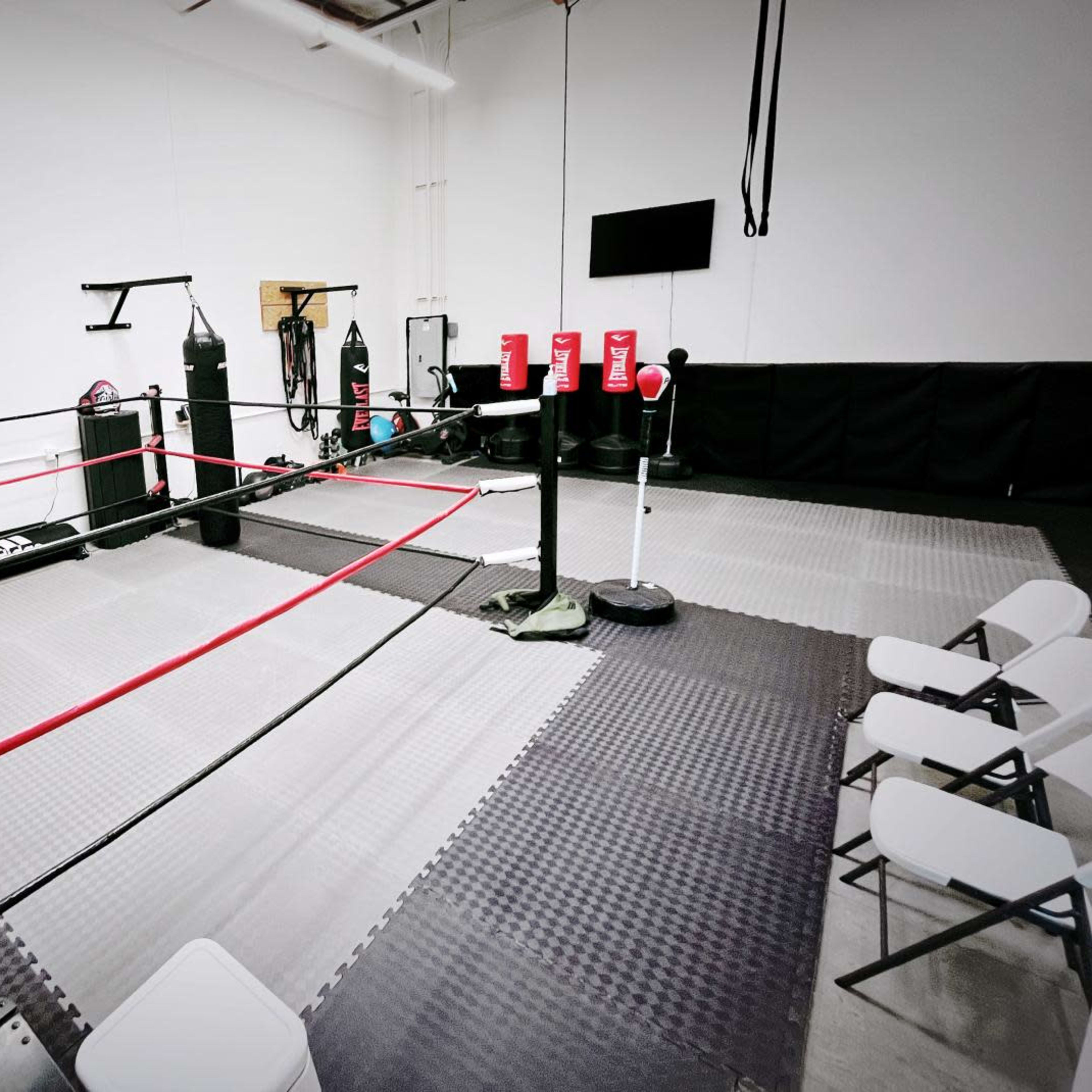 A boxing training area featuring a ring, punching bags, and several chairs arranged nearby.