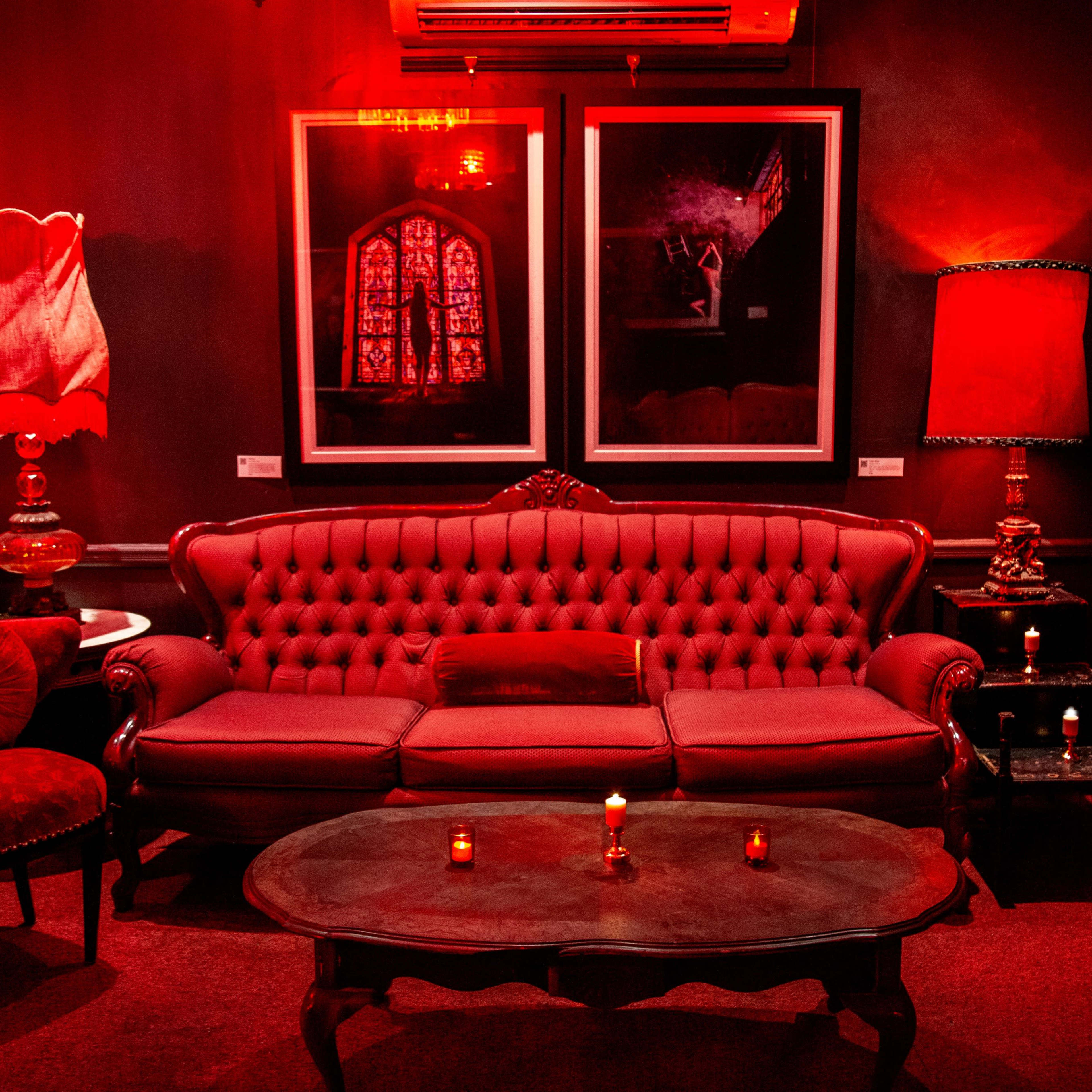 The room features a red-themed seating area with a tufted sofa, a round coffee table, and two lamps, accompanied by framed artwork on the walls.
