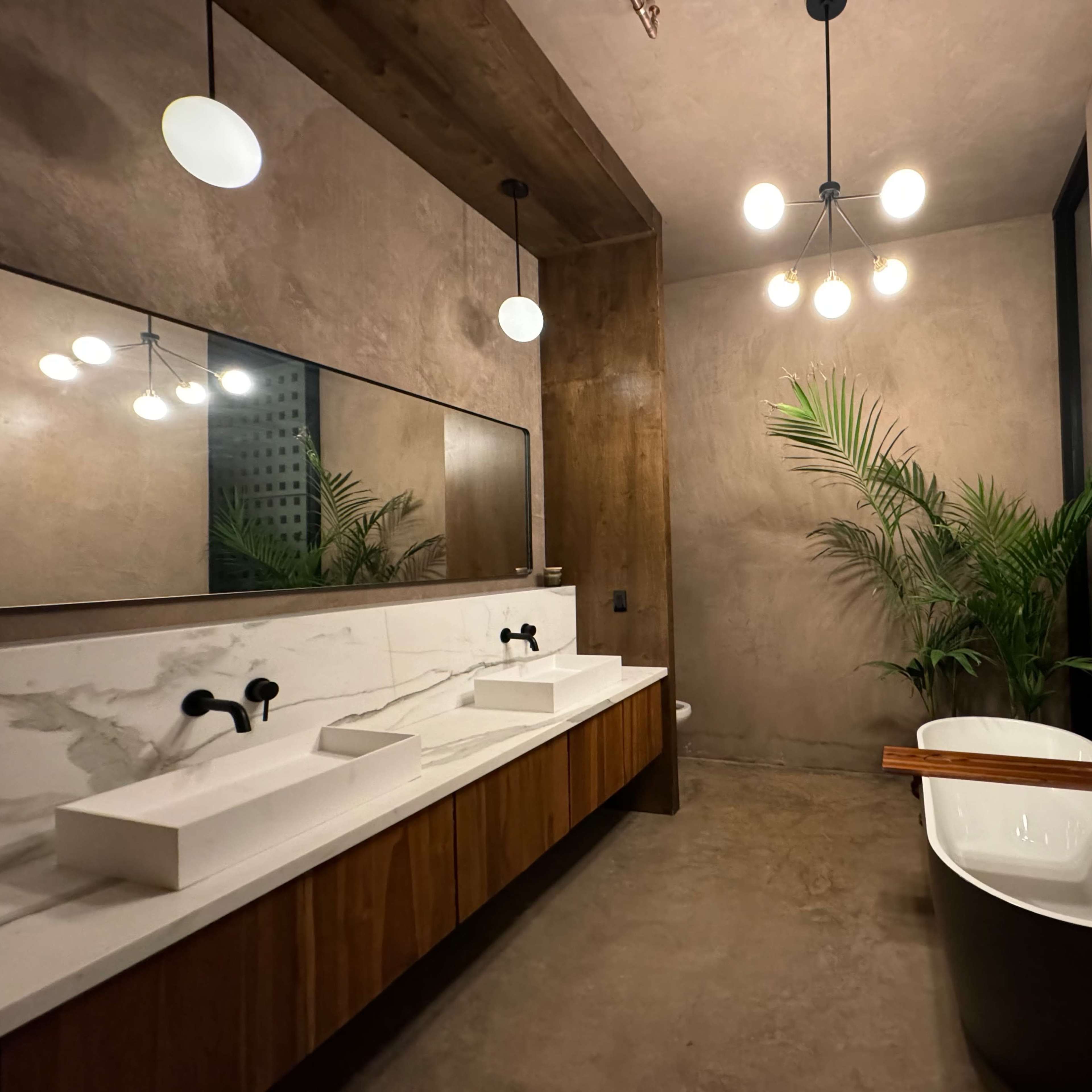 A modern bathroom with a concrete floor, a large mirror above a double sink vanity, a freestanding bathtub, and a potted plant.