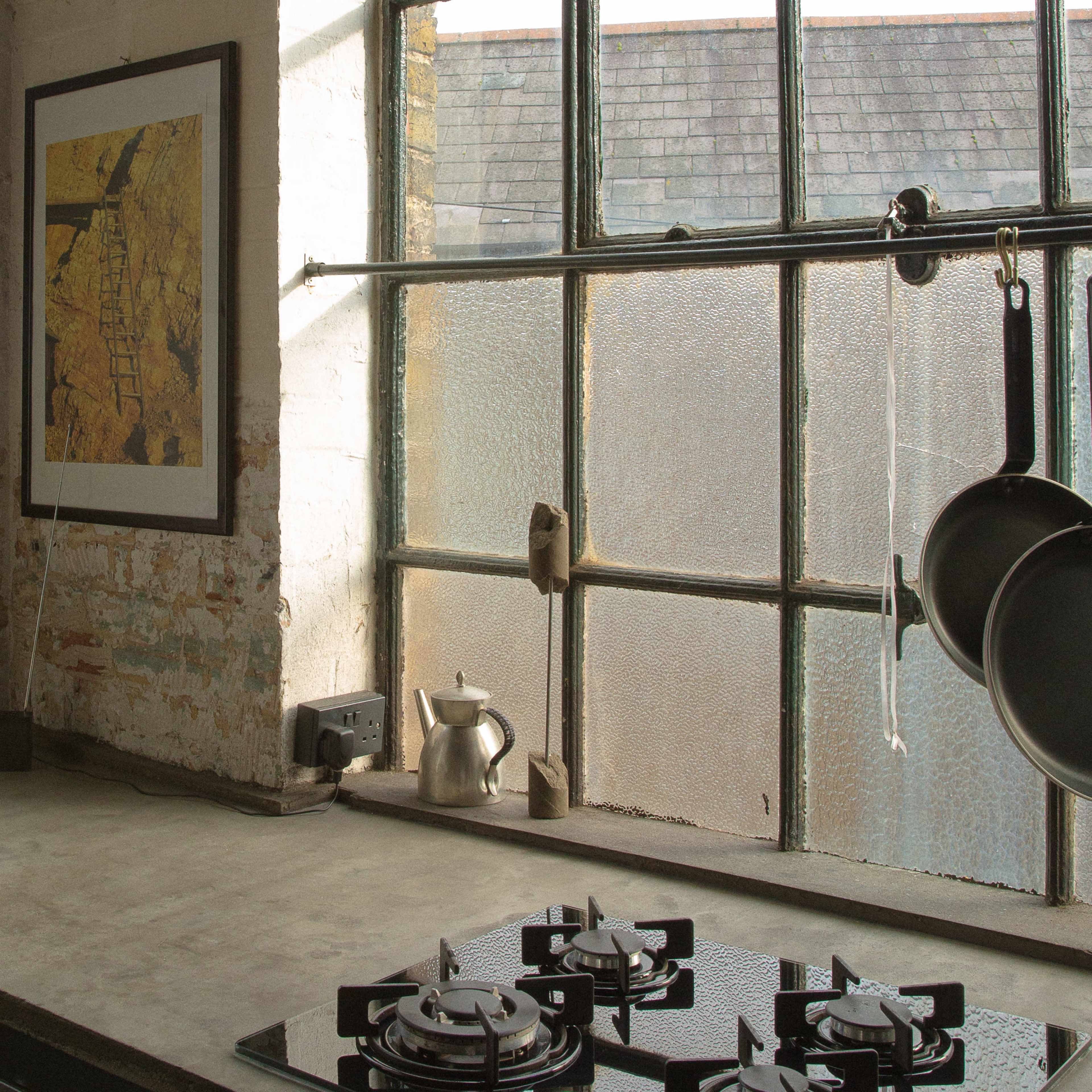 A kitchen features a concrete countertop, a gas stove with multiple burners, and a large window displaying an outdoor view.