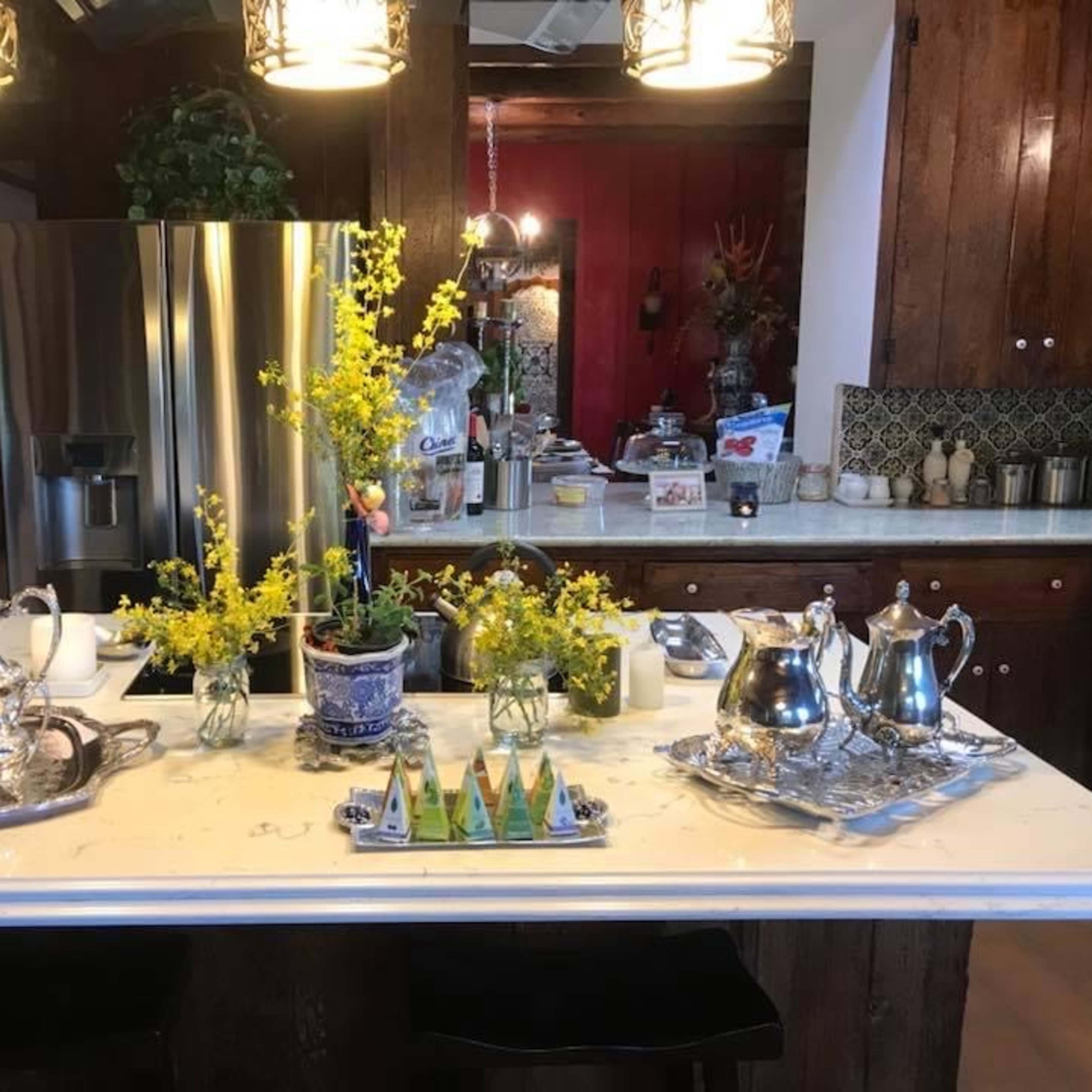 A kitchen island displays a collection of silver teapots, a blue and white vase with flowers, and decorative items arranged on a marble countertop.