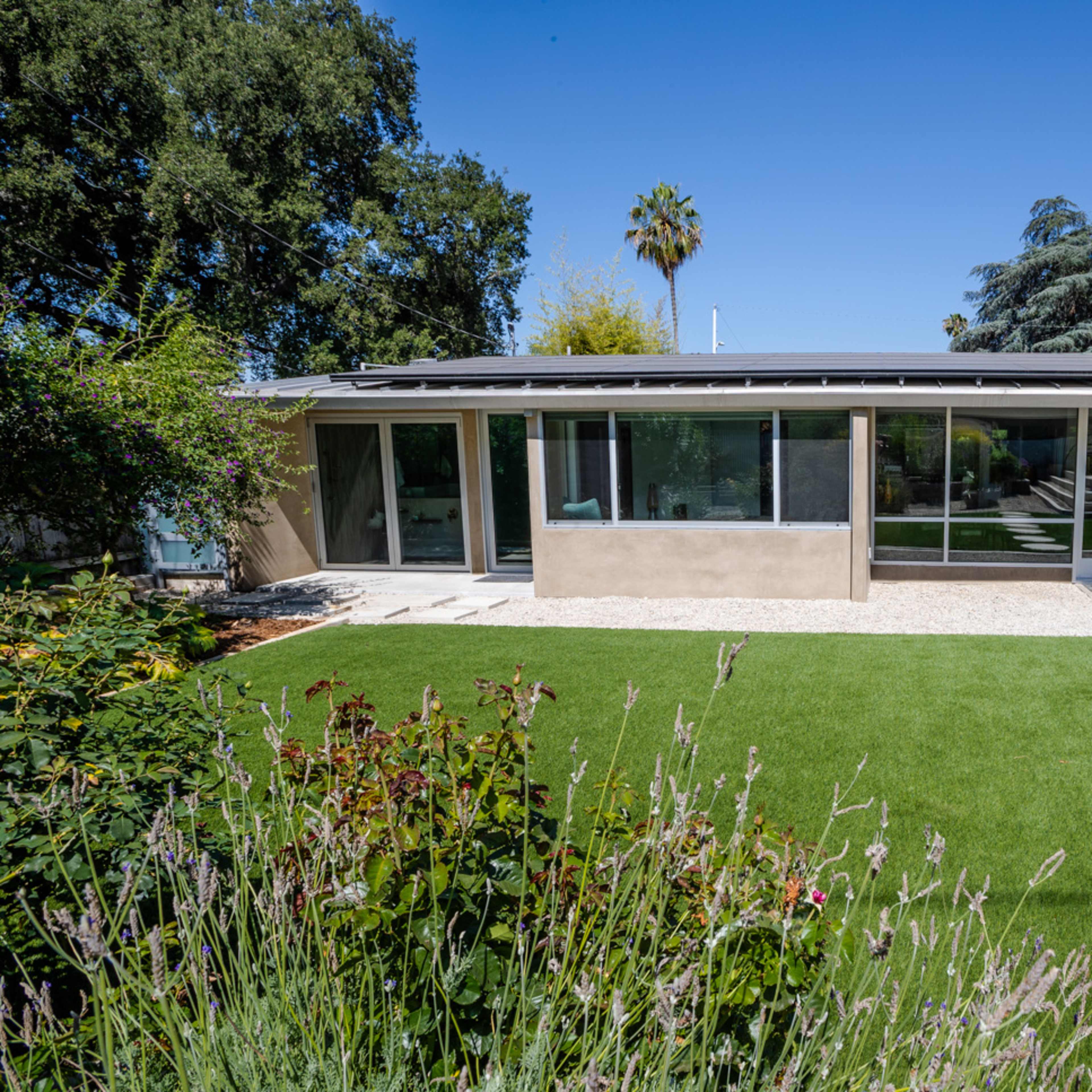 A modern house with large windows and a grassy yard is visible, featuring stepping stones leading to the entrance.