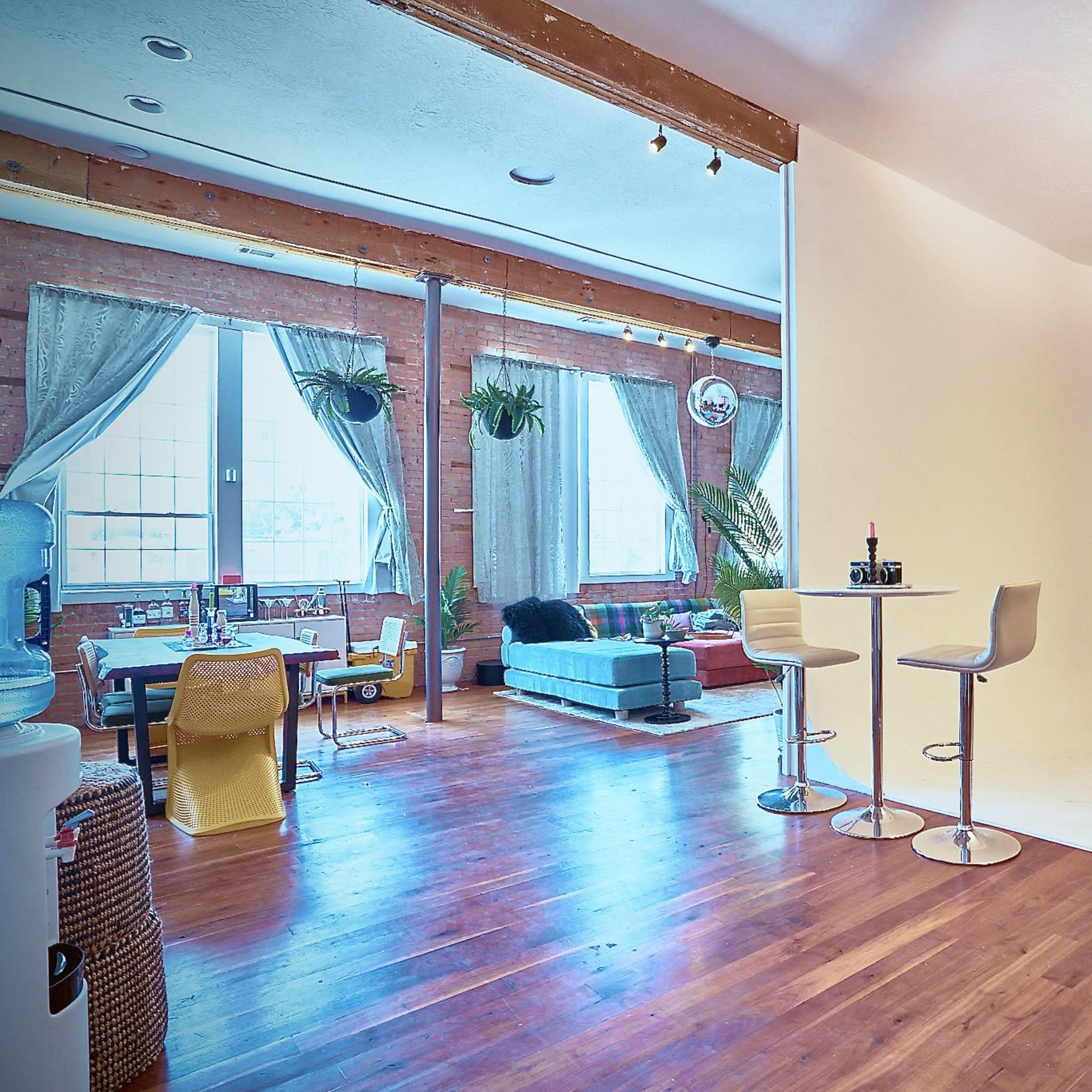 A spacious interior features large windows, wooden floors, a cozy seating area, and a white backdrop for photography.