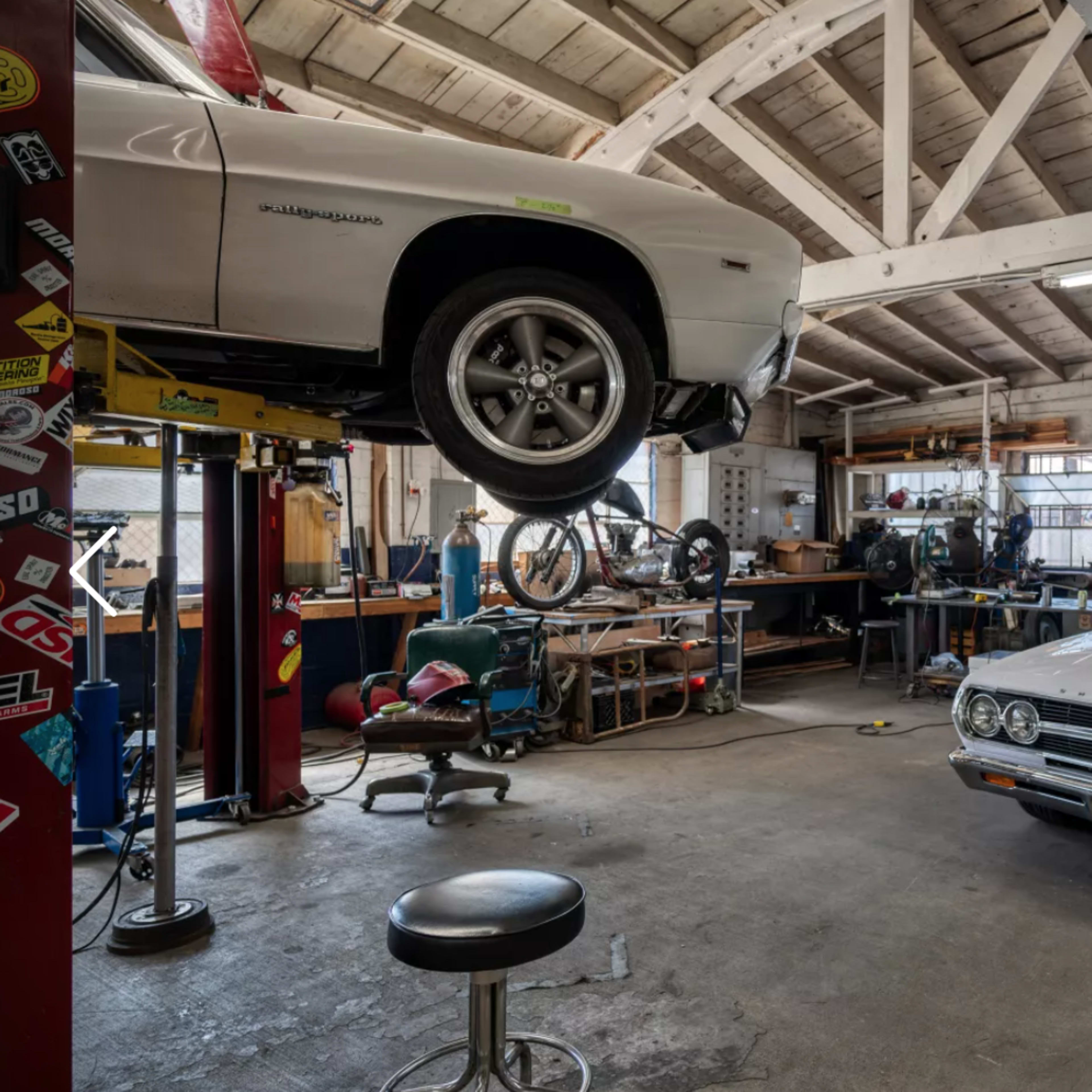 A well-equipped garage features two classic cars, one on a lift and the other parked, surrounded by tools and workbenches.