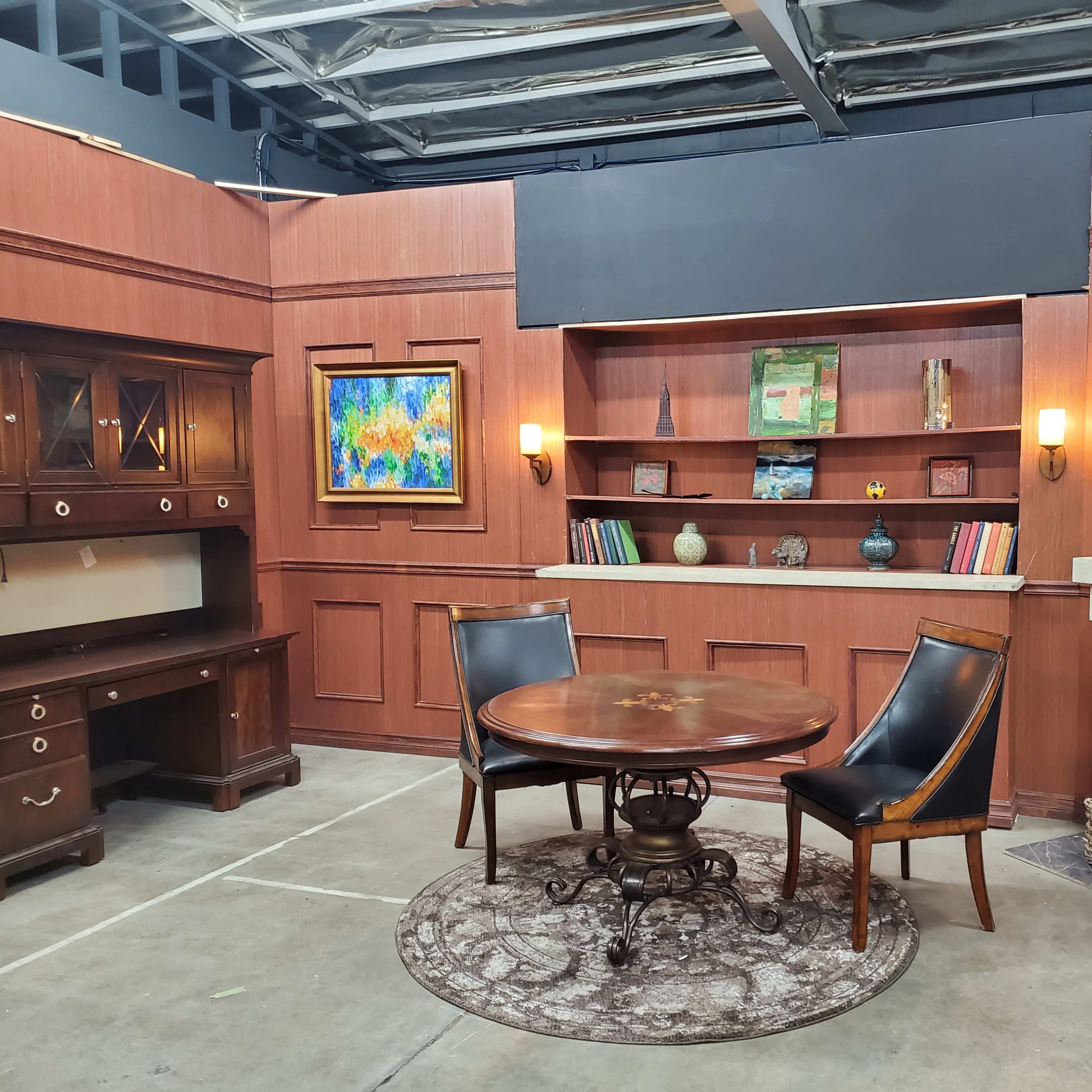A furnished room with a wooden table and chairs, built-in shelves displaying decorative items and books, and a flat-screen TV mounted on the wall.