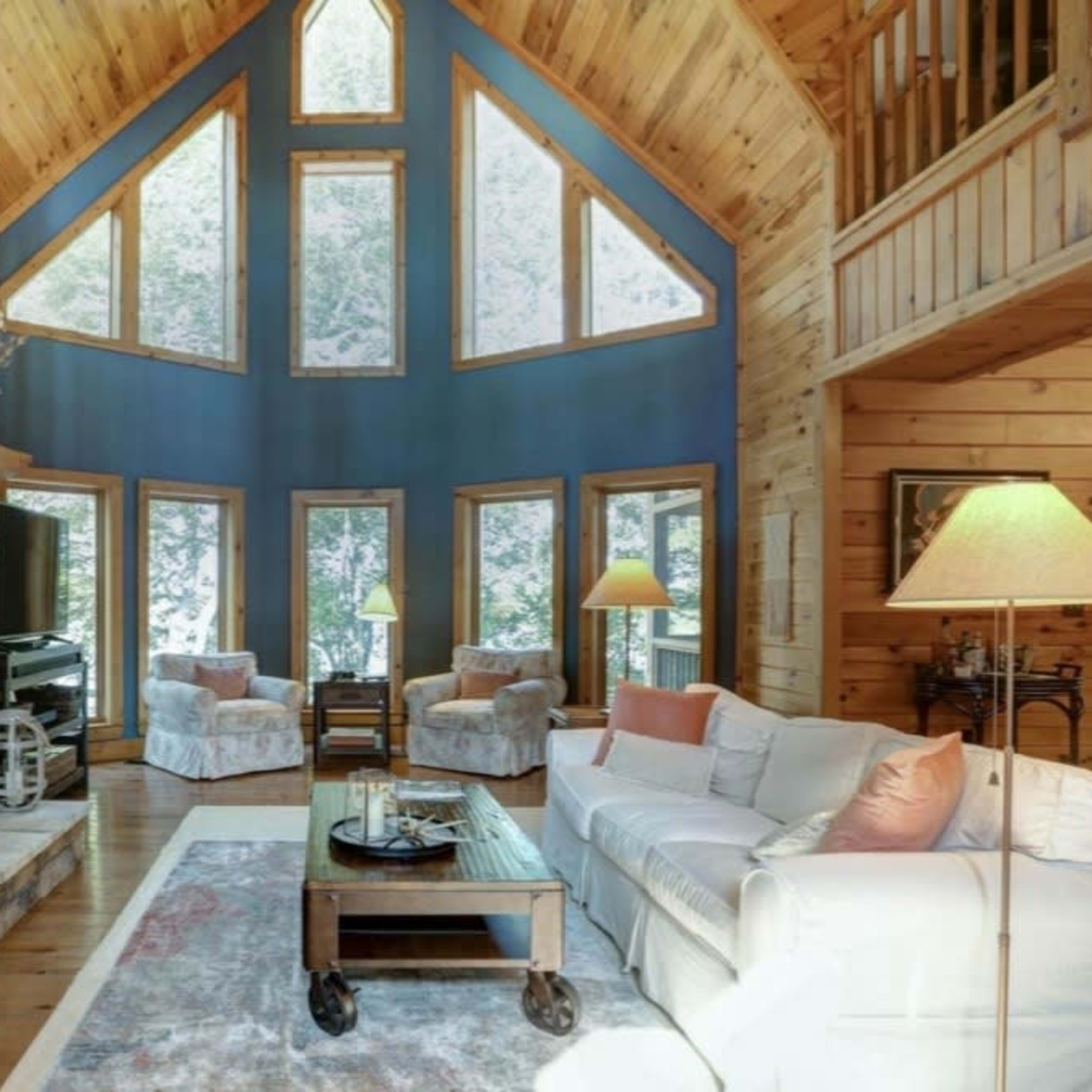 A spacious living room with high ceilings, a stone fireplace, large windows, and wooden accents.