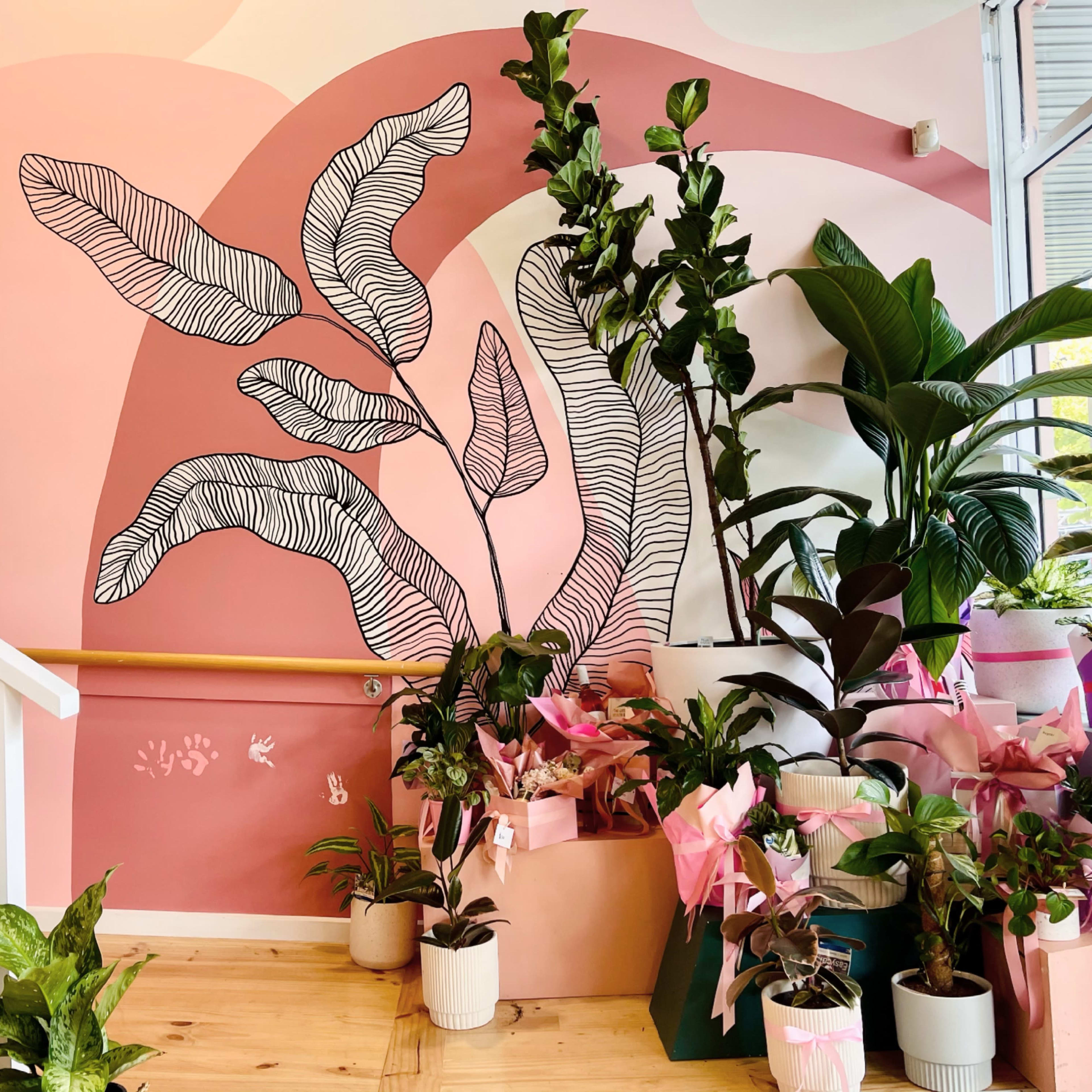 A staircase adorned with a pink and white mural featuring large leaves, surrounded by various potted plants with decorative wrappings.