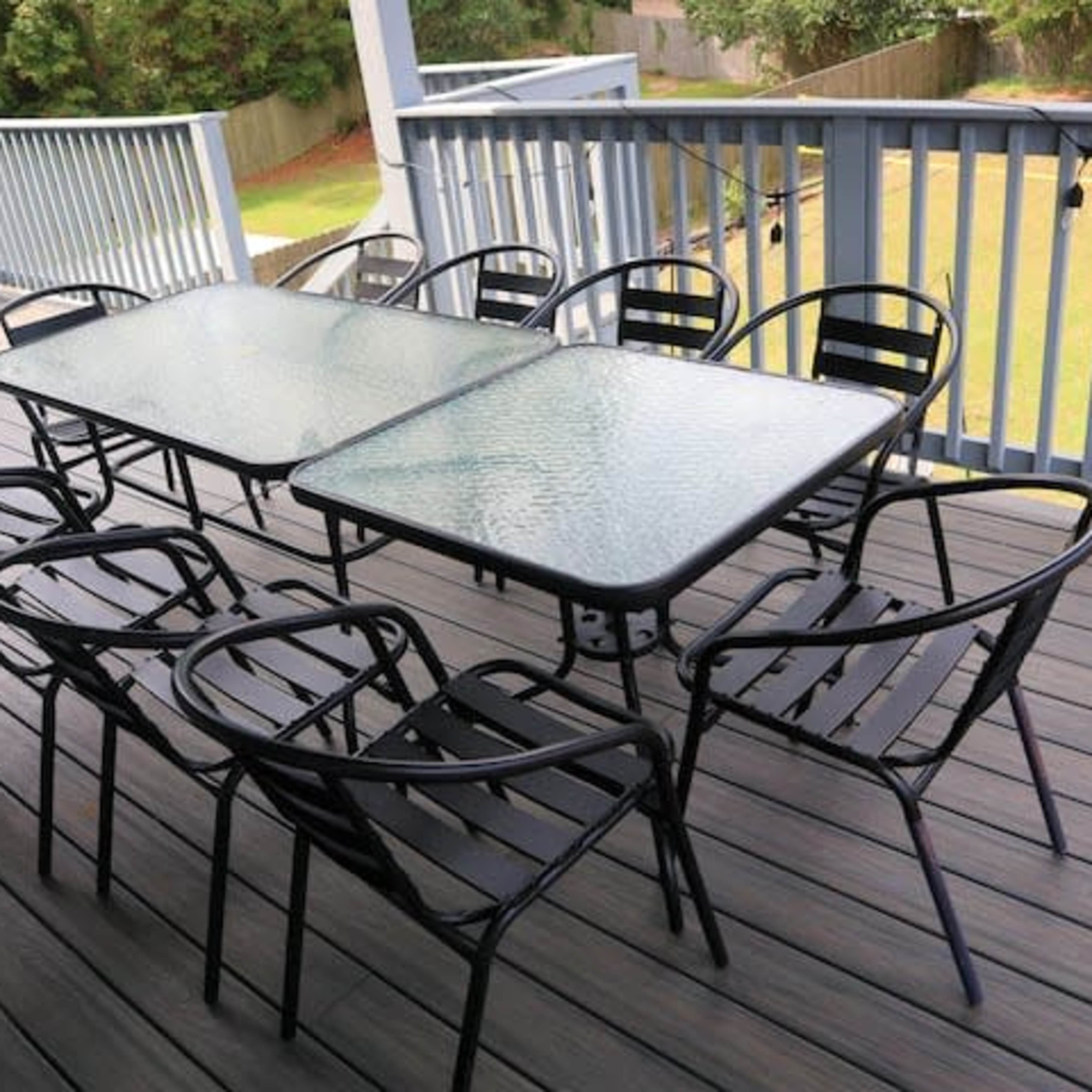 A patio with two glass-top tables surrounded by several black metal chairs.