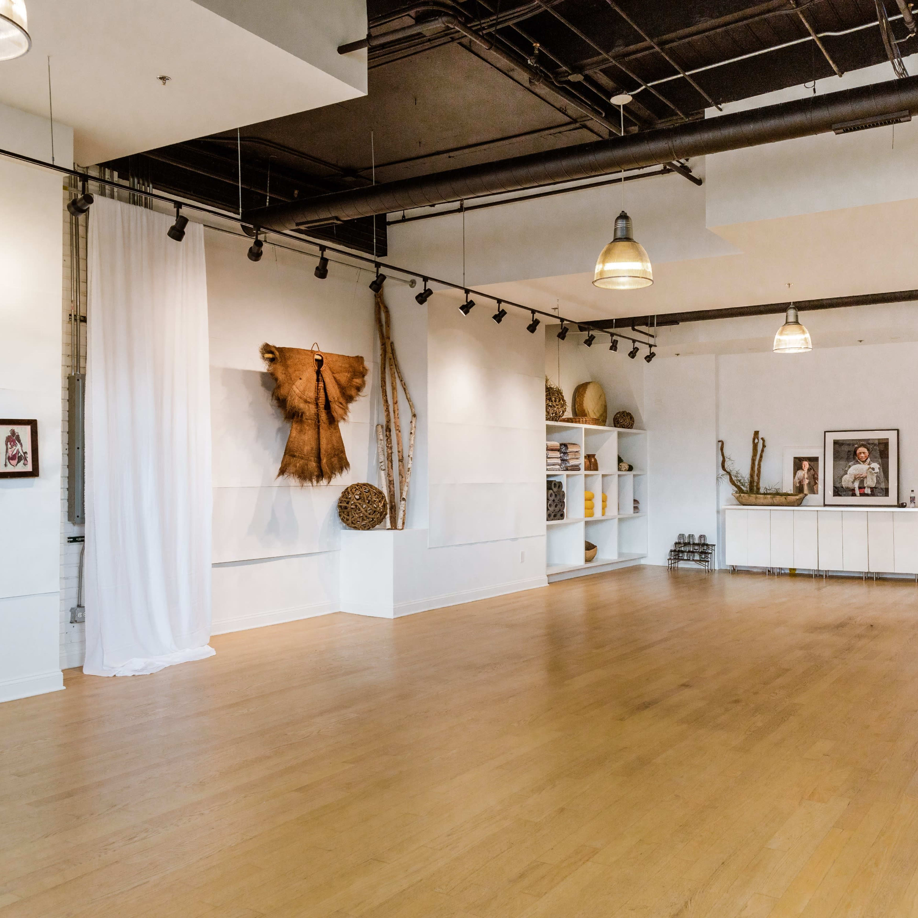 A spacious, well-lit room with wooden floors, art on the walls, and a minimalist white shelf arrangement.
