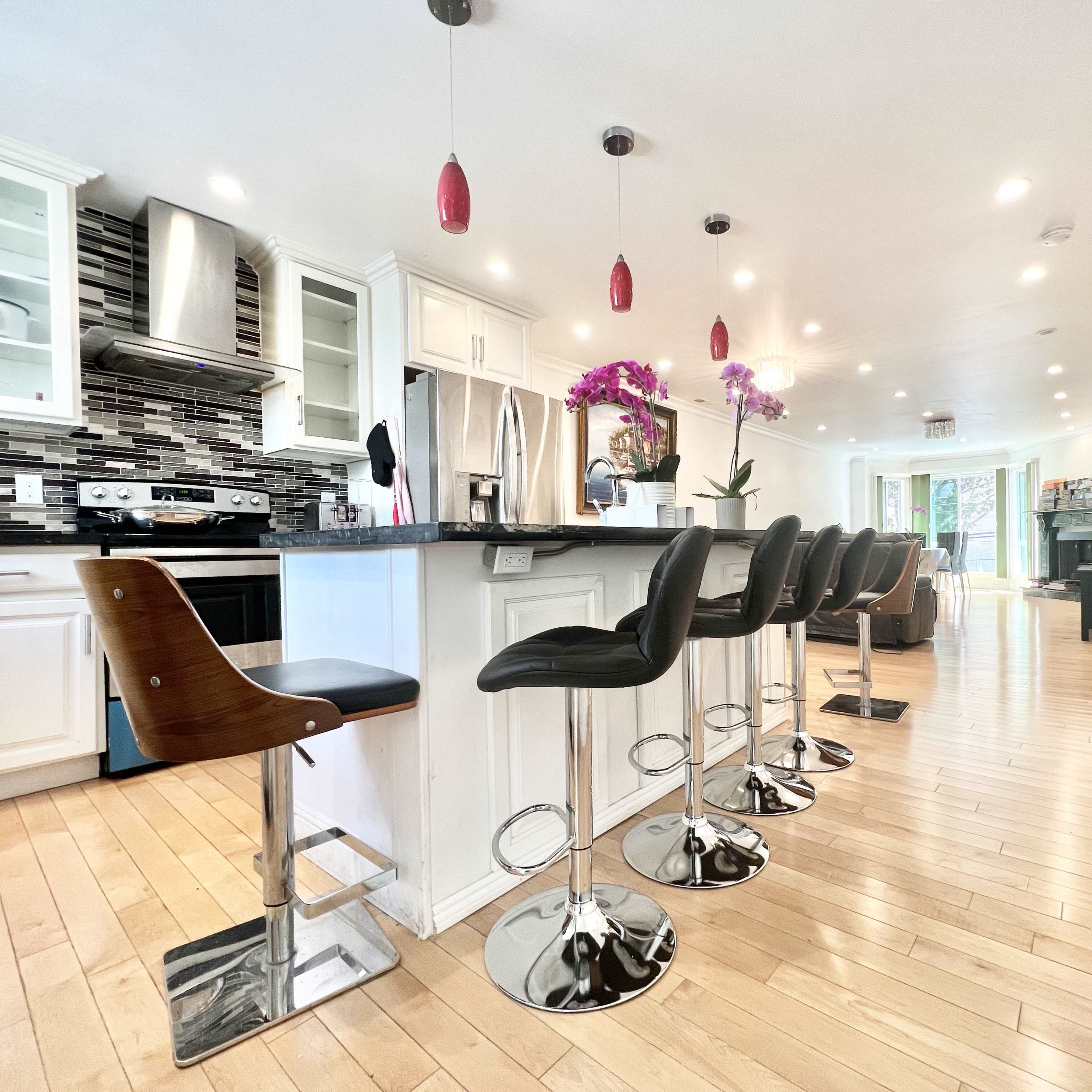 A modern kitchen with white cabinetry, a central island equipped with bar stools, and a spacious living area visible in the background.