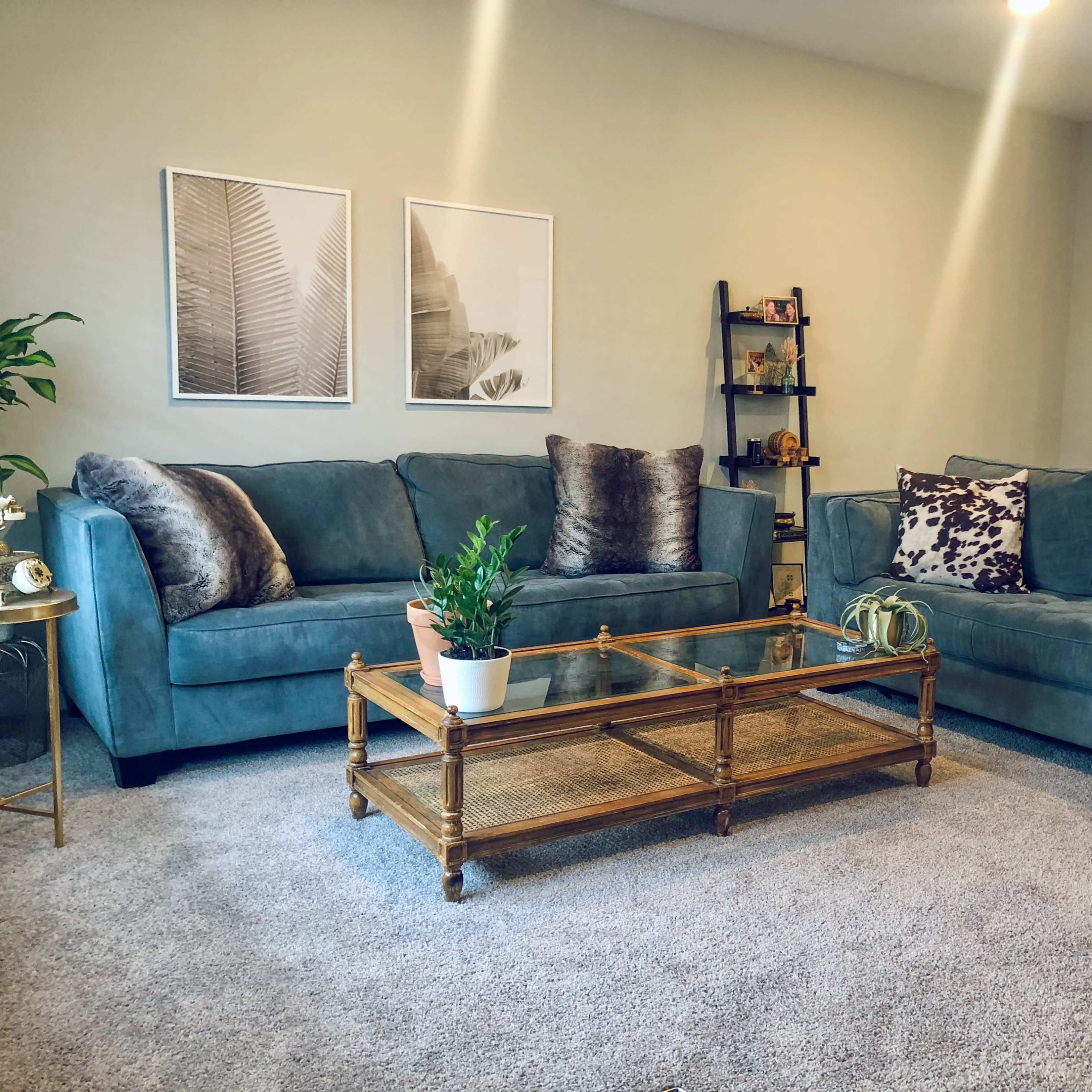A living room featuring a blue sectional sofa and loveseat, a glass-top coffee table, and decorative wall art.