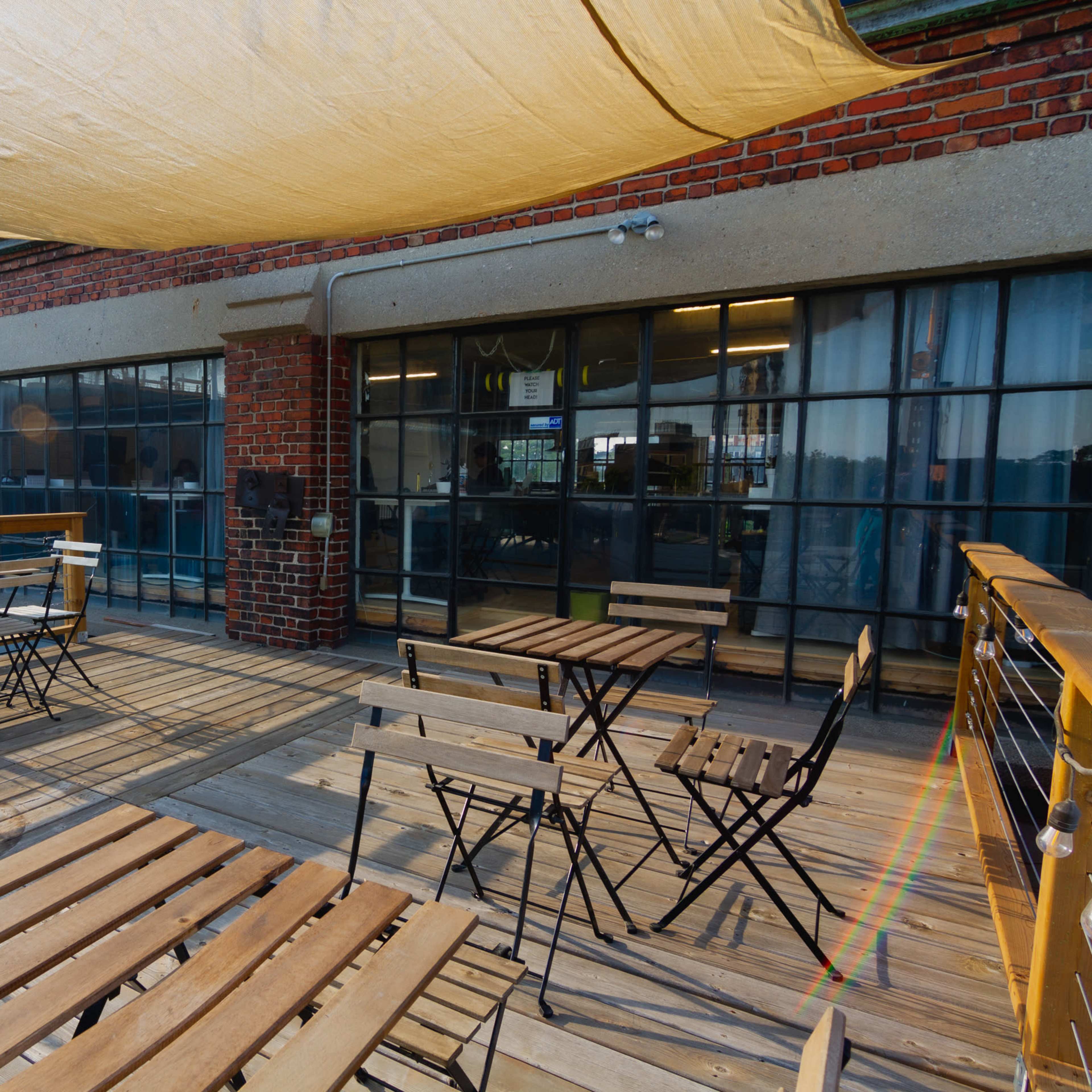 A wooden deck area with several metal-framed tables and chairs under a large fabric canopy.