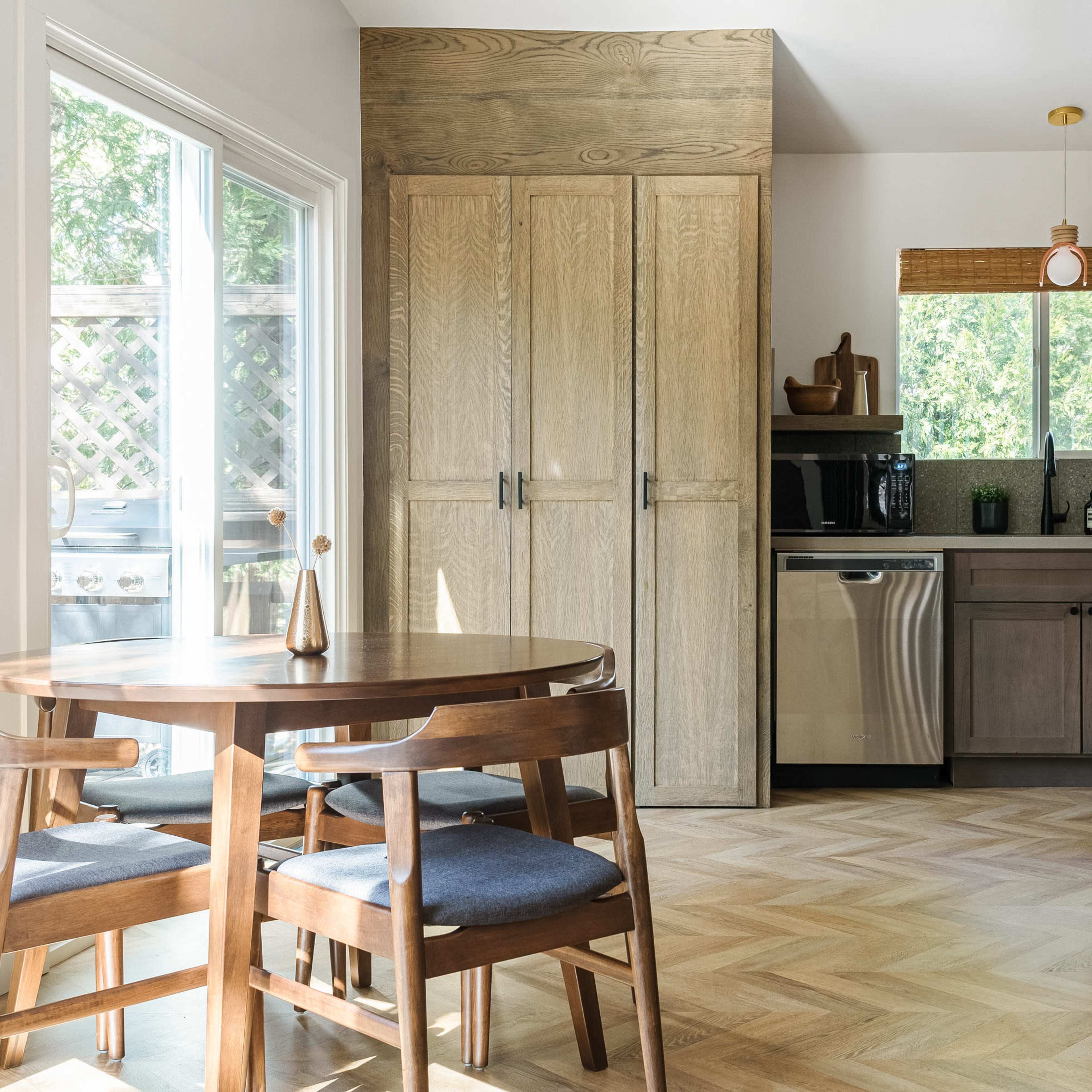 A small dining area features a wooden table with four chairs beside a kitchen with cabinetry and stainless steel appliances.