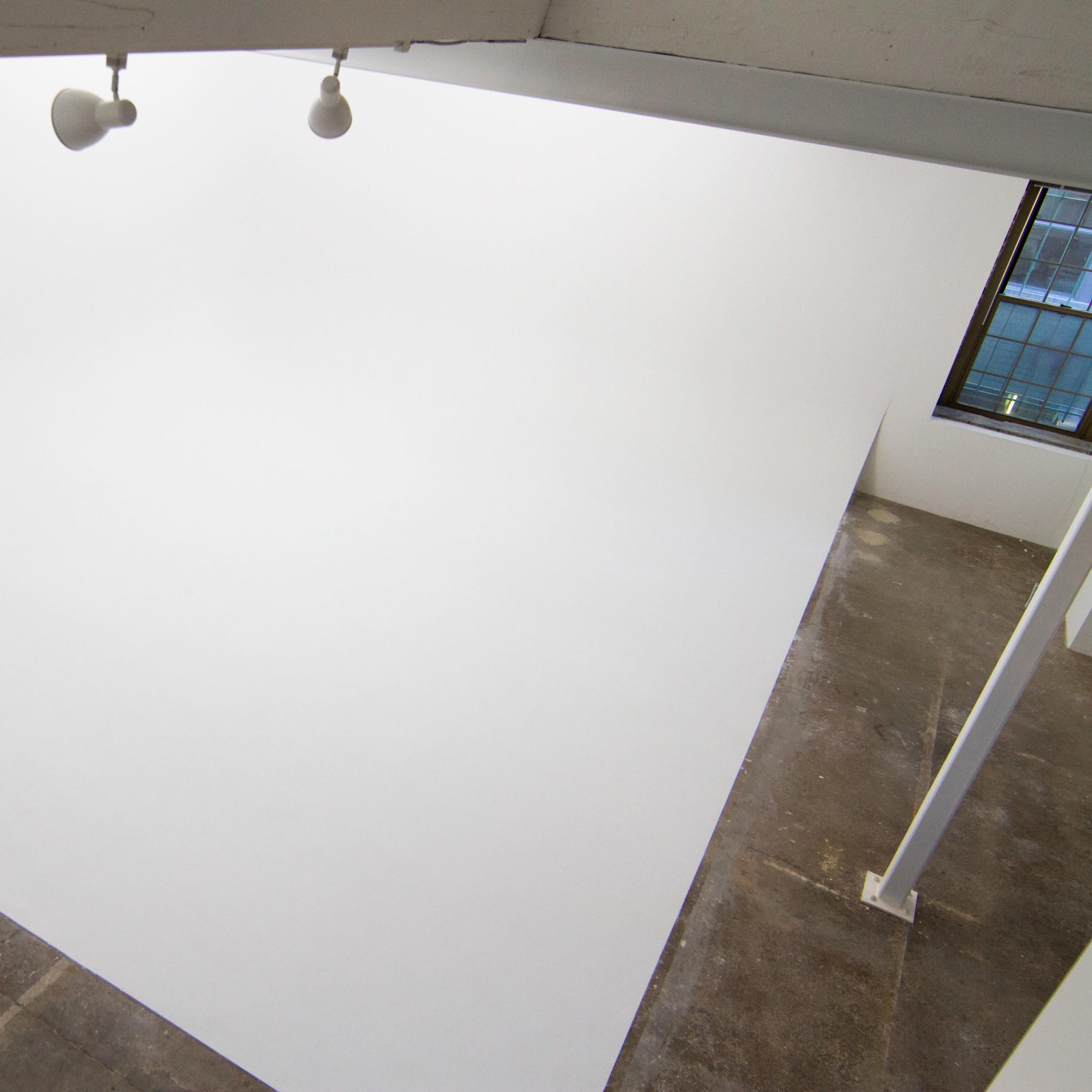 A spacious, empty room with a curved white wall and ceiling, illuminated by overhead spotlights.