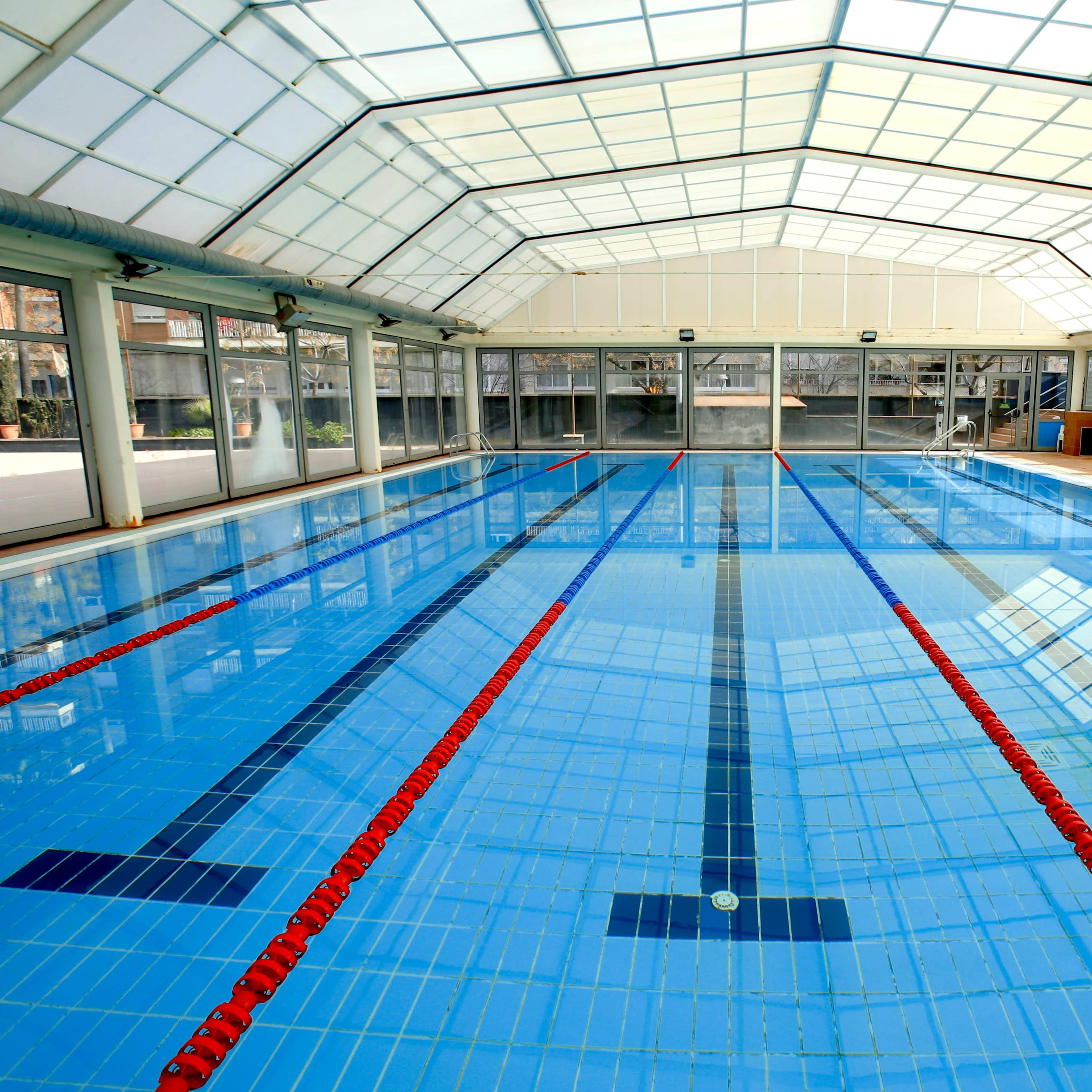 An indoor swimming pool features clear water, lane markings, and a glass roof that allows natural light to enter.