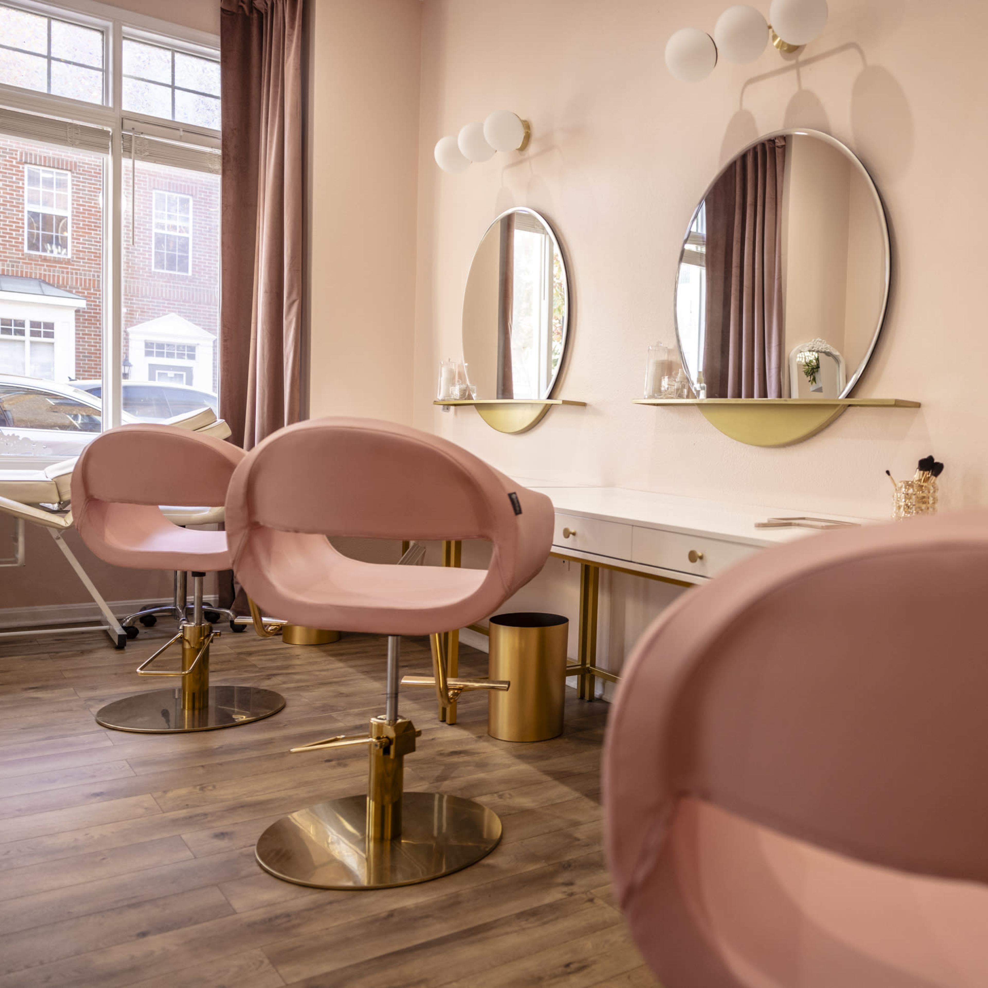 A beauty salon interior with pink chairs and three round mirrors above a white vanity.